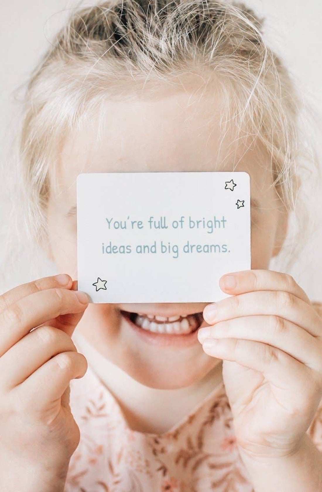 A young girl holding up a card that says "you're full of bright ideas and big dreams".