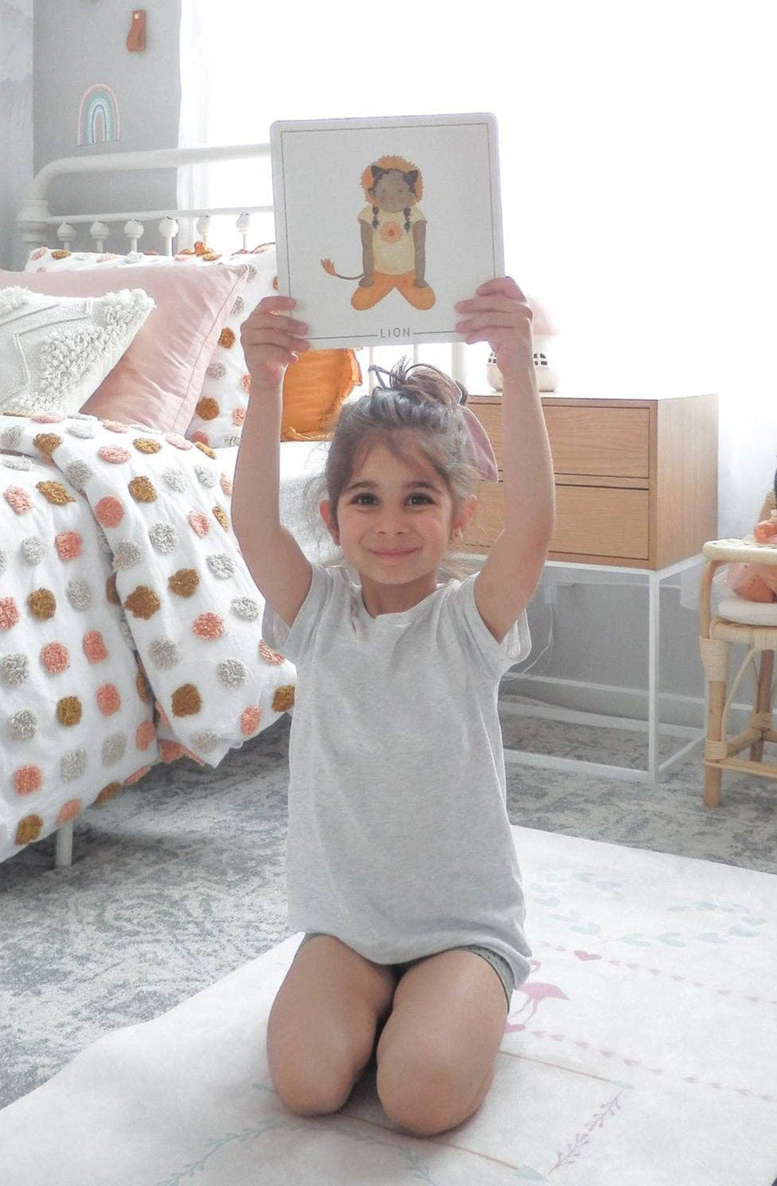 A young girl holding up a yoga flash card above her head in her bedroom.