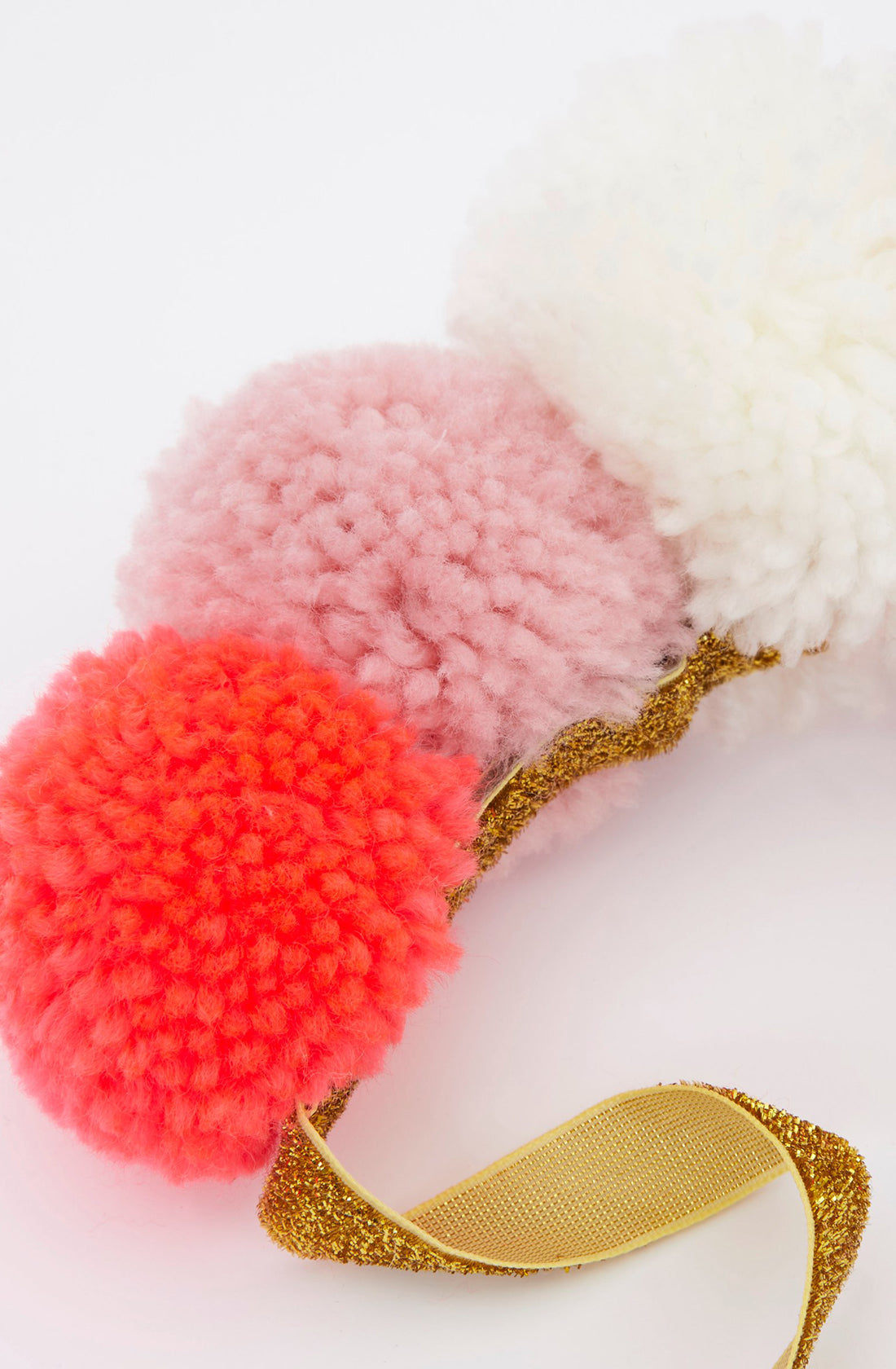 The Pom Pom Crown by MERI MERI is a gold glitter elastic headband adorned with three fluffy pom-poms in red, light pink, and white. Perfect for a dressing-up costume, the pom-poms are positioned in a row on top of the headband against a white background.