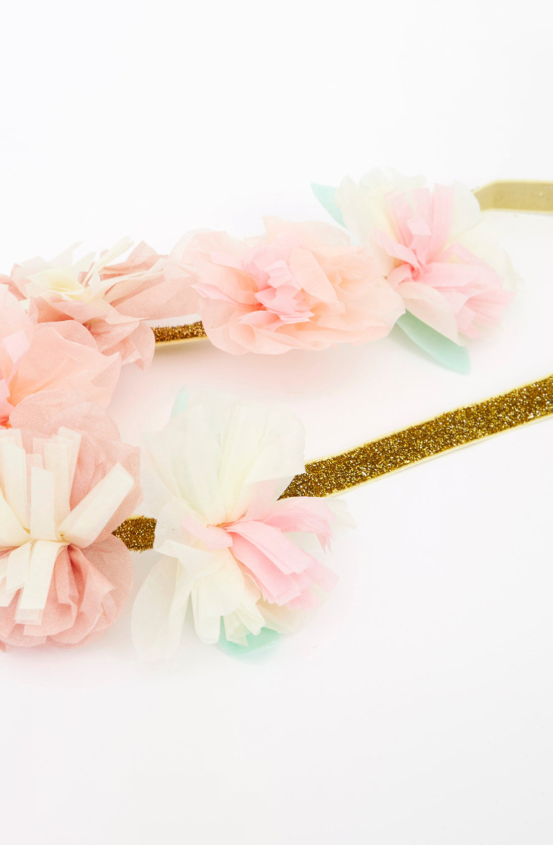 A close-up of a Blossom Party Crown from MERI MERI, featuring pastel-colored tissue paper flowers in shades of pink, white, and light blue. The delicate blooms are attached to a sparkly gold band, making it perfect for princess parties. The background is plain white.