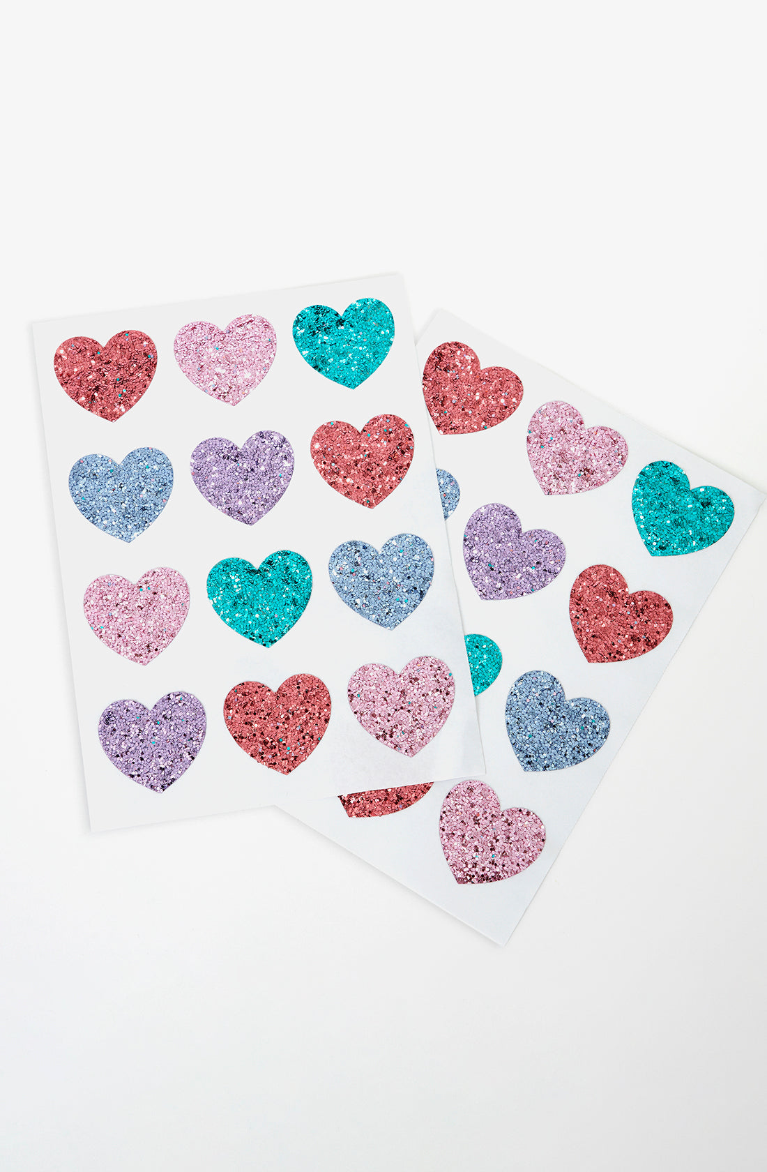 Two sheets of Rainbow Glitter Heart Stickers by MERI MERI are displayed against a white background. Each sheet features hearts in pink, purple, blue, and red glitter. The hearts are arranged in a grid with three hearts per row and five rows on each sheet—perfect for Valentine’s Day crafts.