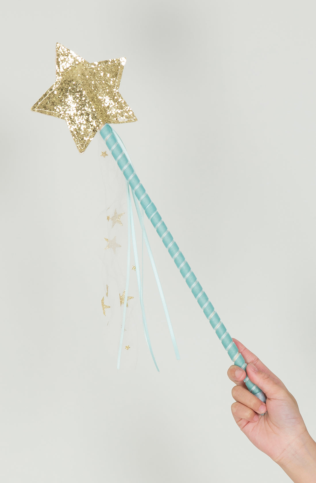 A hand holds the MERI MERI Tulle Star Wand Mint, featuring a magical star with a sparkling gold top. The wand's handle is elegantly wrapped in light blue ribbon, and several light blue and white ribbons adorned with small gold stars dangle beneath the star. Perfect for any fairy or princess dress-up box, the background is plain white.