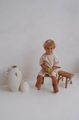 Boy sitting on timber stool wearing the essential matching set in sand