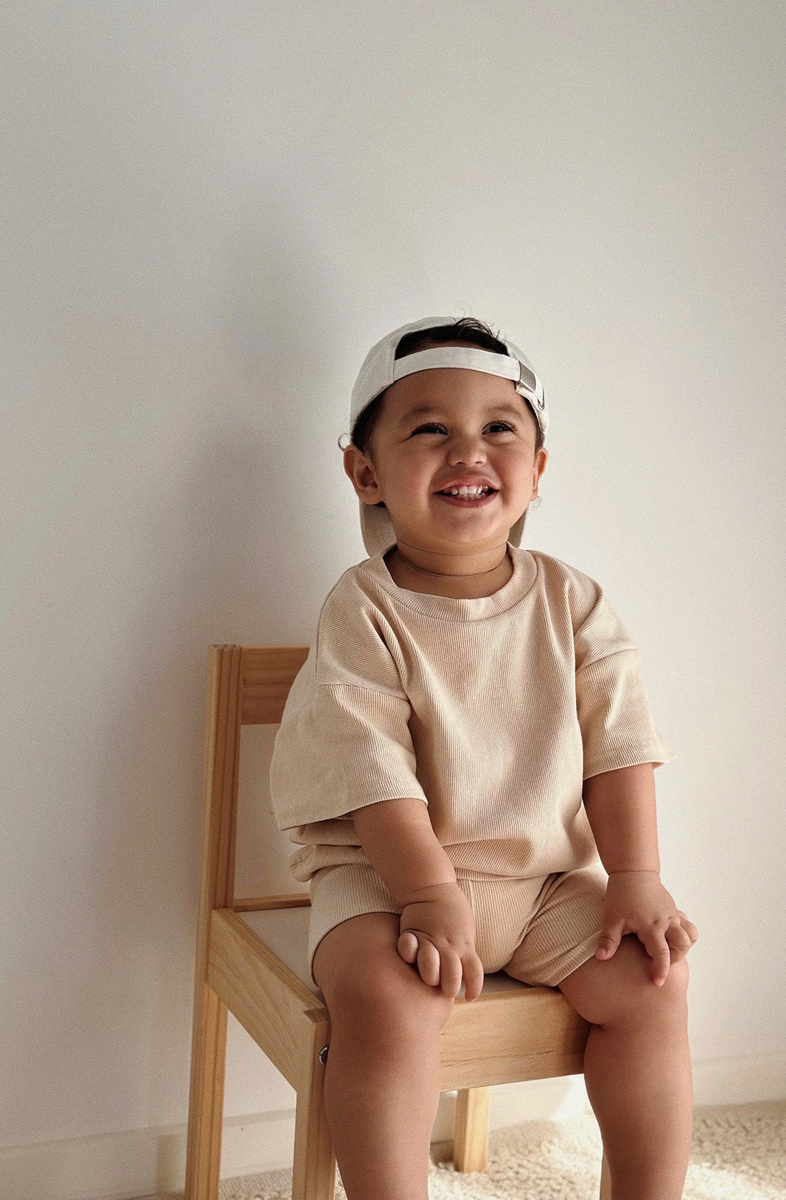 Boy sitting on chair wearing a cap backwards and the essential set in sand