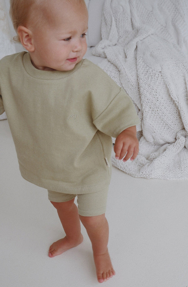 Boy standing on floor wearing the matching essential set in sage