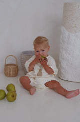 Baby wearing the Pear romper while sitting on the floor eating a pear