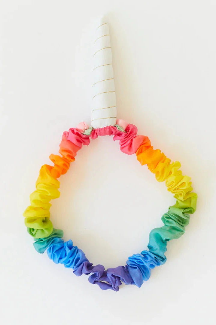 The Rainbow Unicorn Headband by SARAH'S SILKS, ideal for dress-up play, showcases a vibrant array of colors and is adorned with a spiraled white horn, set against a plain background.