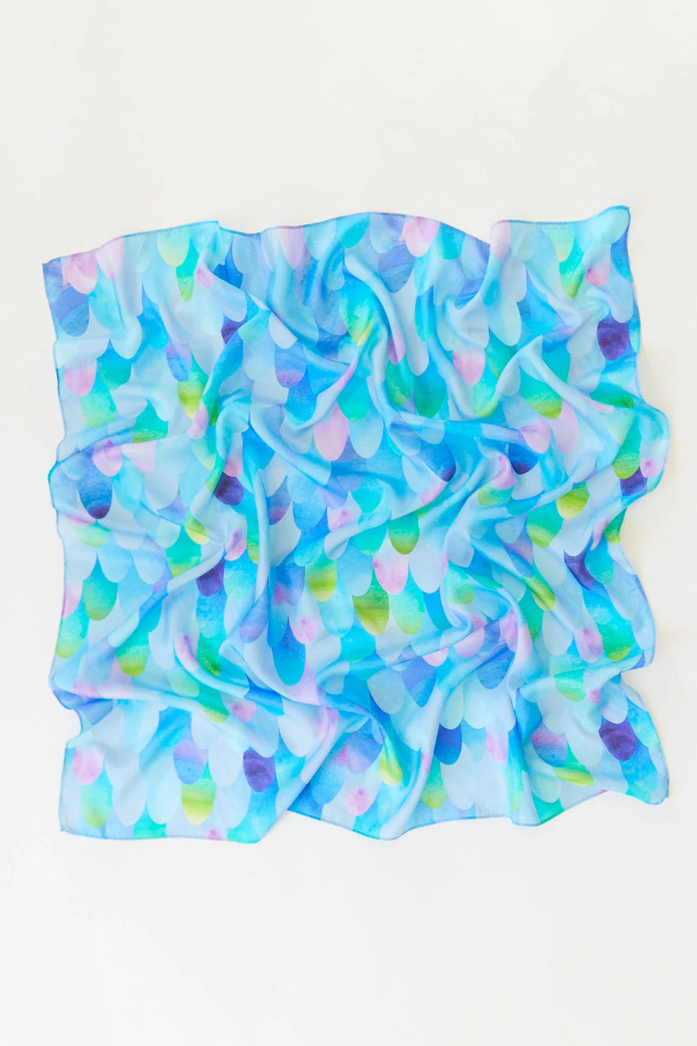 The Blue Dragon Playsilk by SARAH'S SILKS is a crumpled, colorful scarf crafted from 100% pure silk. It showcases a pattern of overlapping, semi-transparent scales in shades of blue, purple, and green against a white background. Ideal for open-ended play as part of the enchanting Magical Creatures Playsilks collection.