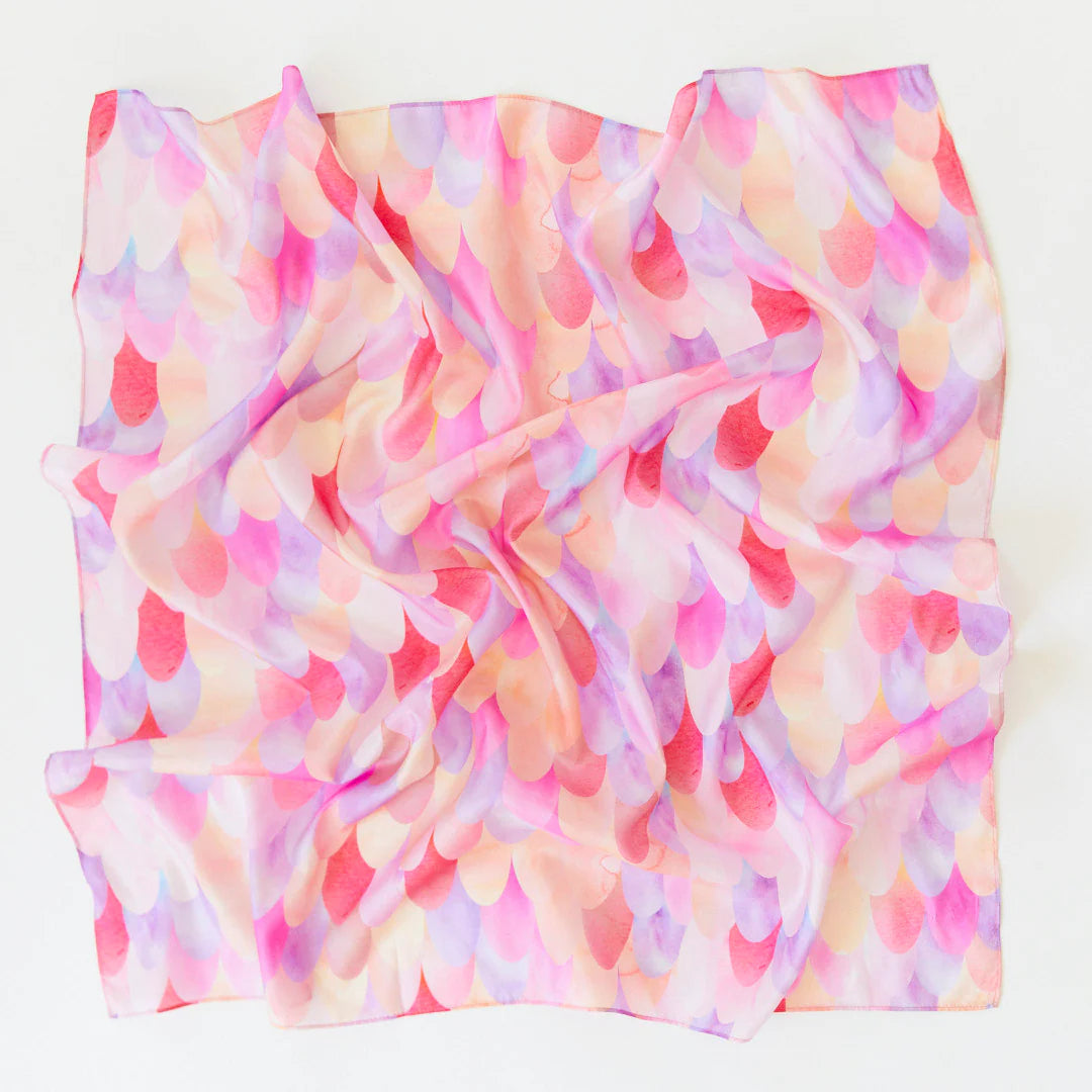 SARAH'S SILKS introduces the Pink Unicorn Playsilk, a vibrant square scarf featuring a pattern of overlapping scales in pastel hues of pink, purple, and yellow. Ideal for open-ended play, it effortlessly becomes an accessory or complements the Magical Creatures Playsilks collection.