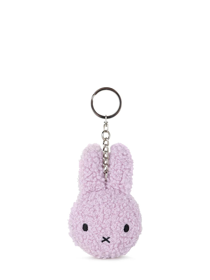 The Bon Ton Toys - Miffy Flat Keychain Tiny Teddy Lavender by BON TON TOYS X MIFFY is a plush, textured lavender bunny head keychain made from recycled polyester, with black stitched features and a silver keyring—ideal for adding cuteness to your backpack.