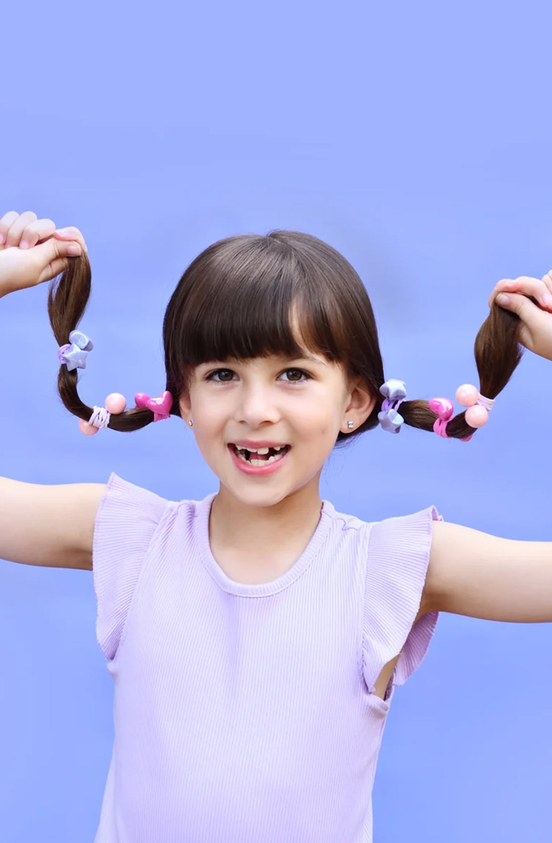 A young girl holding up her pony tails on each side of her head with the no nasties fairy tale bobbles in them.