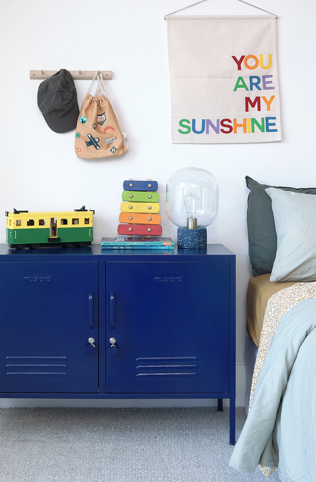 The lowdown locker in navy next to a bed with a lamp and tops on it.