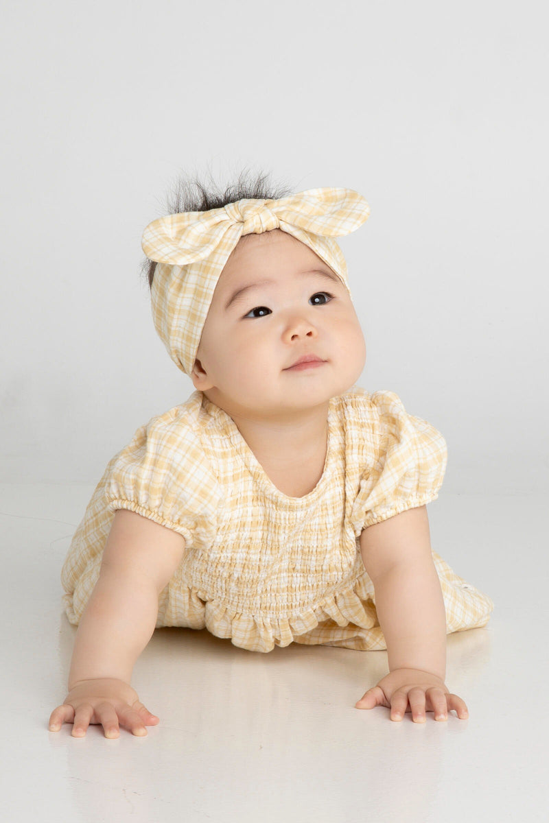 Crawling baby wearing matching headband and dress in sandcastle check