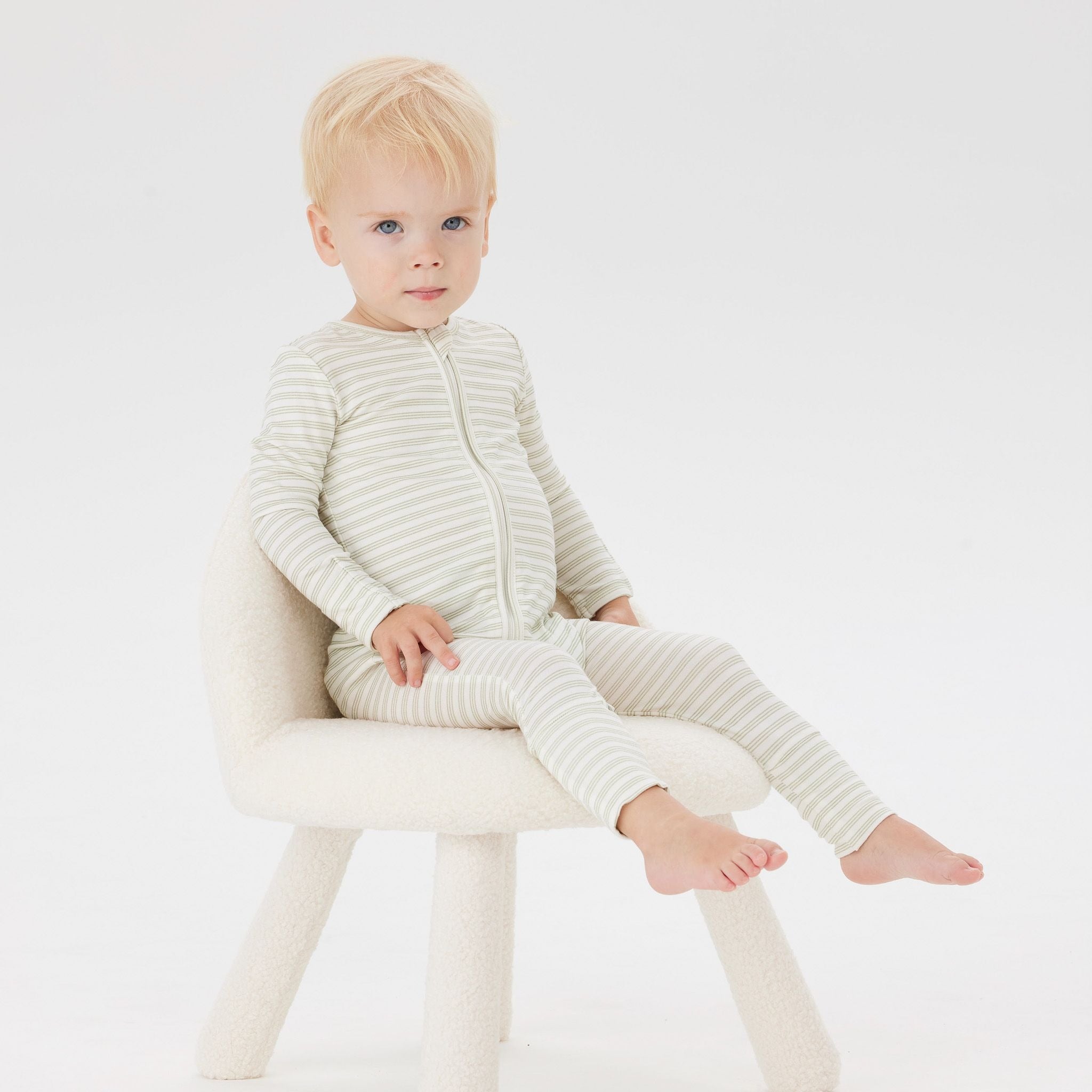 A Toddler wearing the Day or Night Onesies Sage Stripe sitting on a chair.