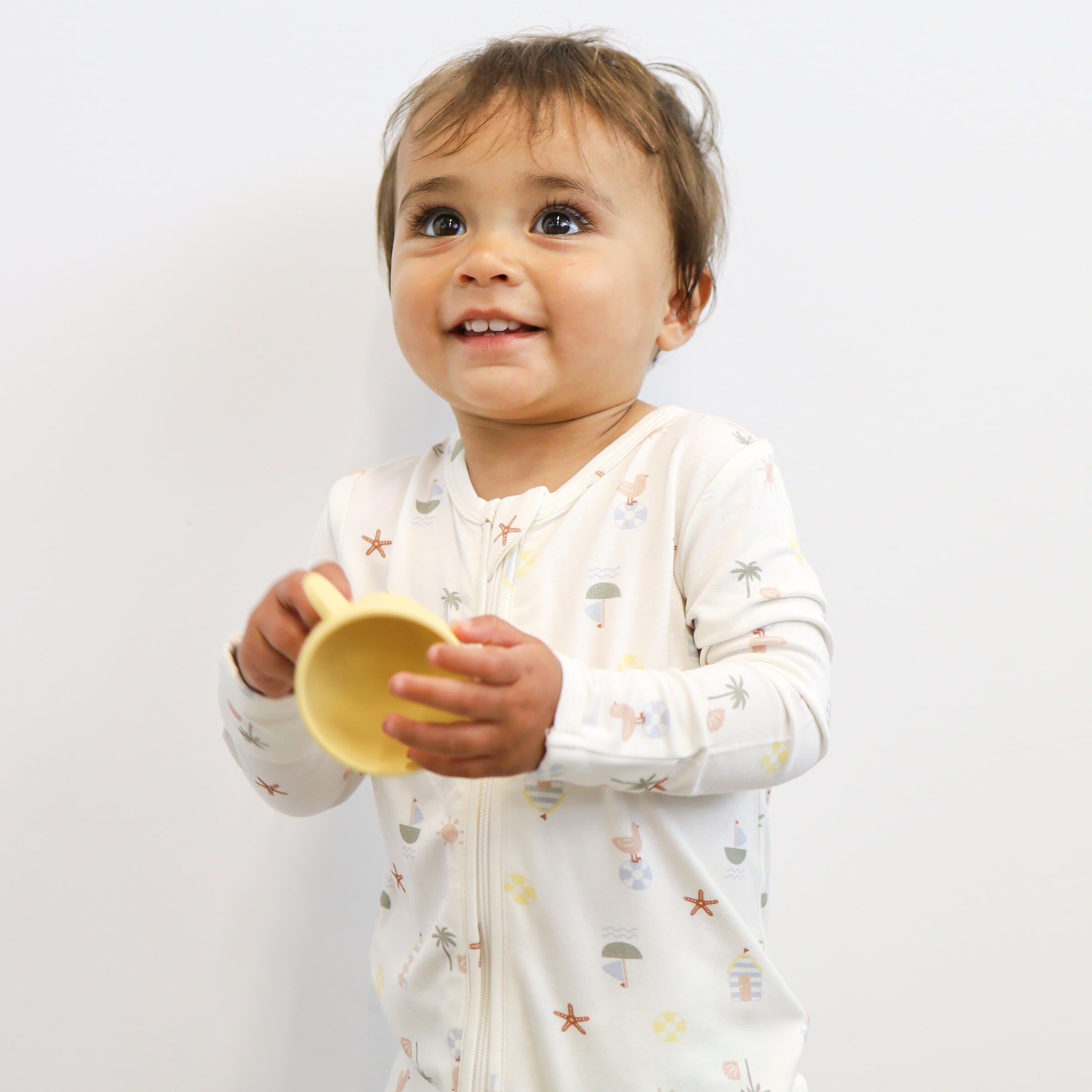 A Toddler wearing the Day or Night Onesies Vacay holding a cup.