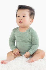 Baby sitting on a mat wearing the comfy bodysuit in  gumnut spot