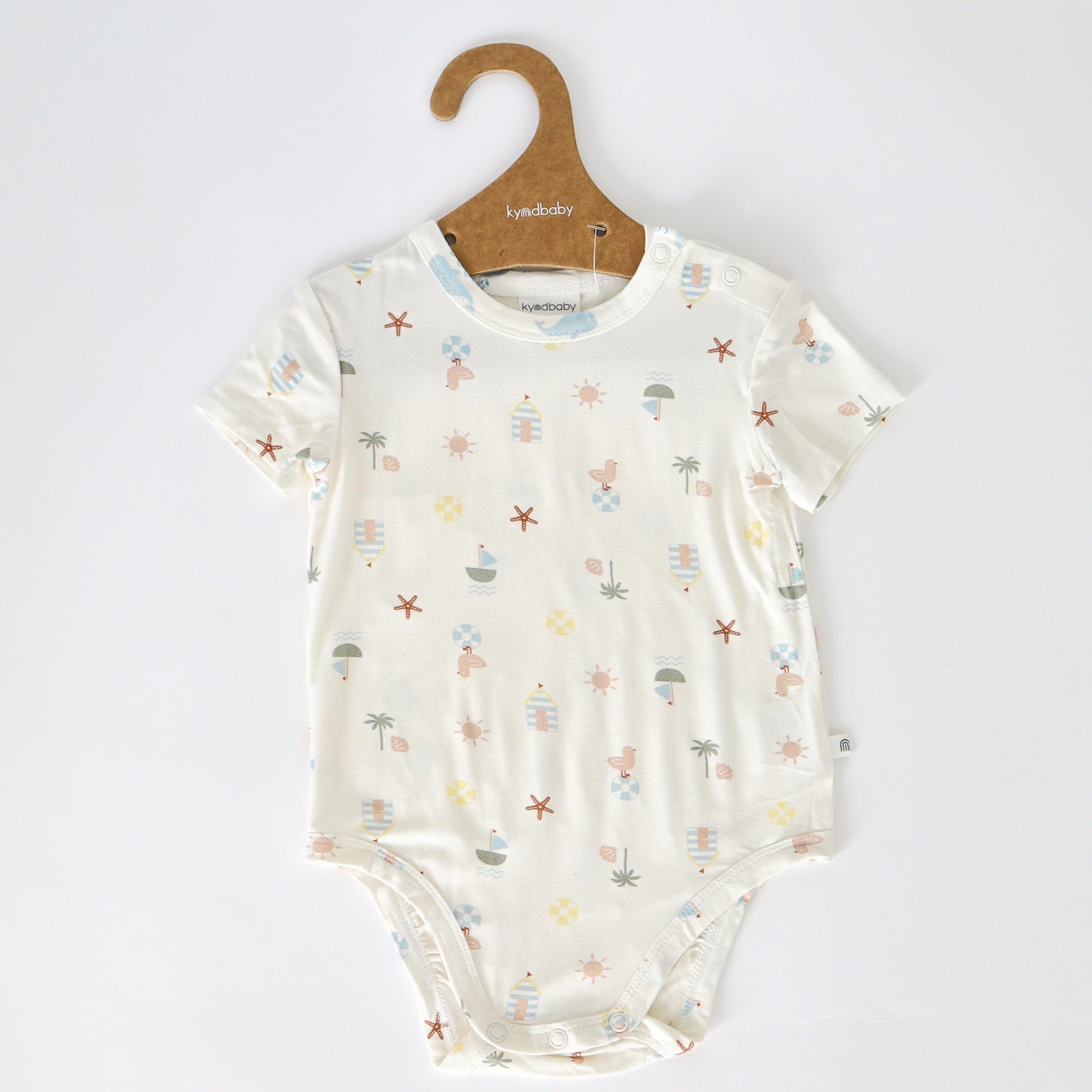 The KYND BABY Comfy Bodysuit Short Sleeve Vacay hanging on a brown coat hanger.