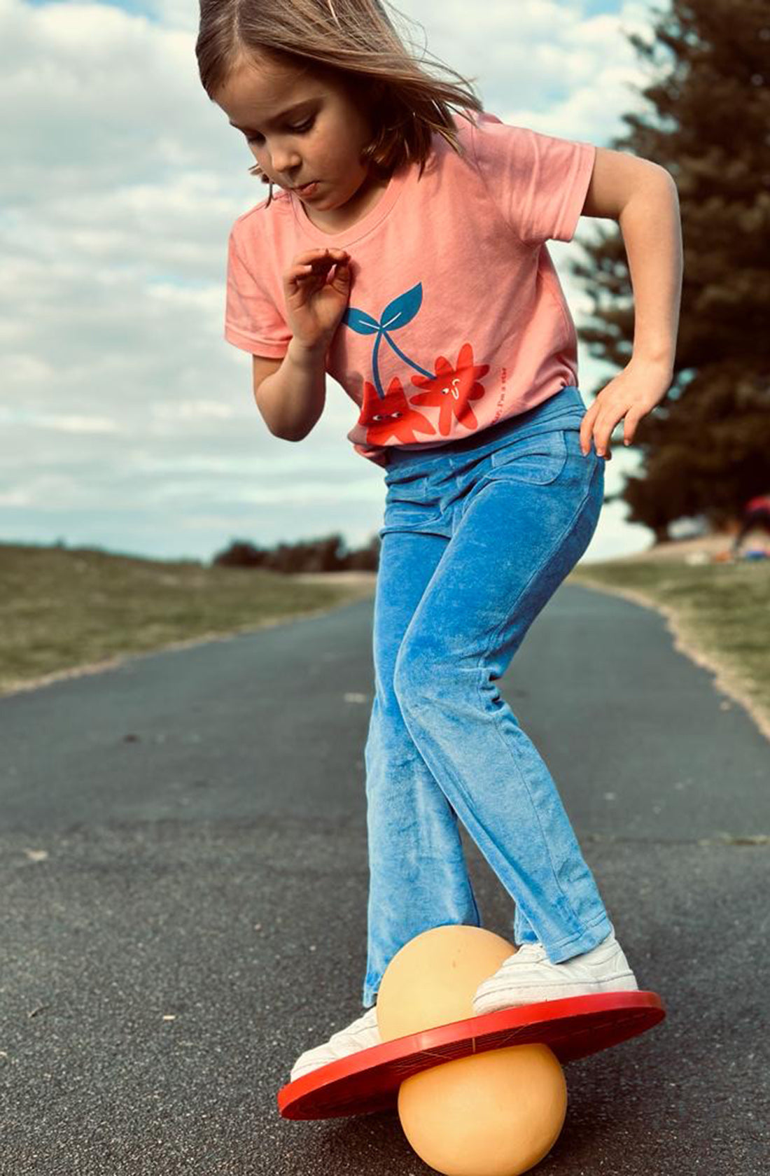 A young girl wearing the PLAYetc
Velour Flares Denim Blue with a peach tee and white sneakers standing on a balance board.