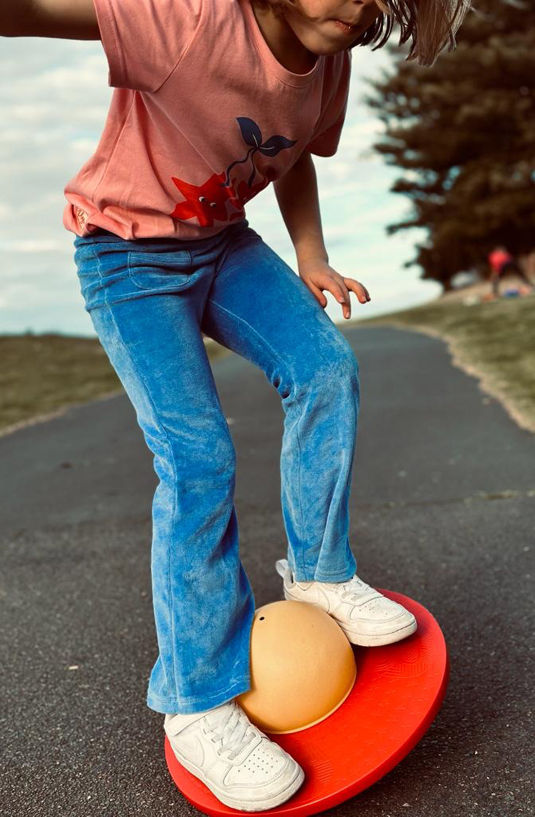 A young girl weaaring the PLAYetc
Velour Flares Denim Blue with a peach top and white sneakers balancing on a balance board outside.