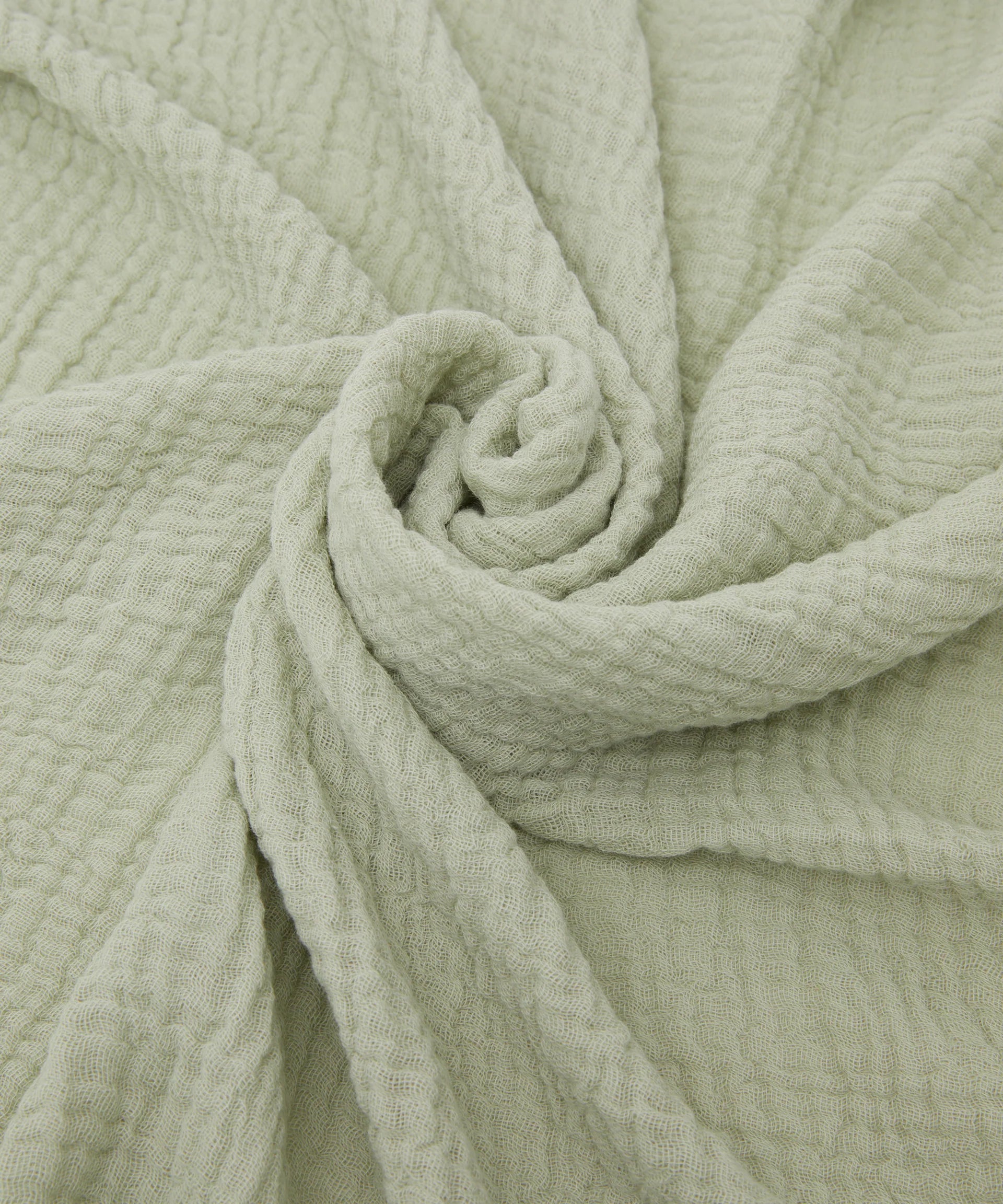 The Swaddle Sage by PHILÉ features Oeko-Tex Certified Cotton in a light green, waffle-textured pattern. Its circular design creates cozy folds and shadows reminiscent of a muslin wrap.