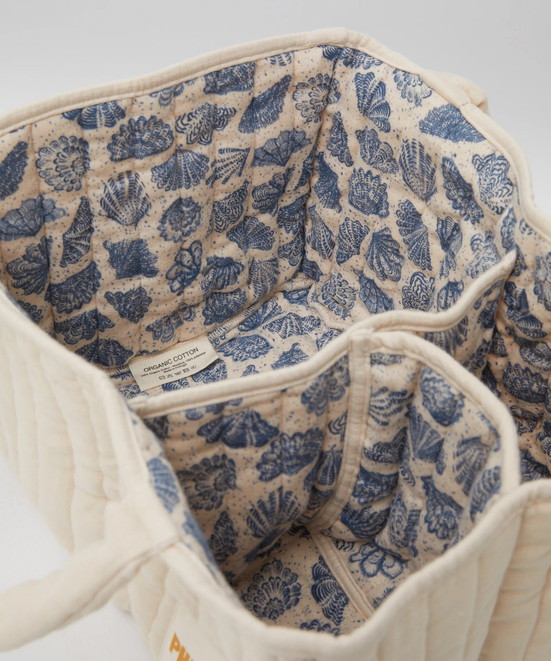 Experience elegance with the PHILÉ Nappy Caddy. This cream quilted bag from the Oceanides Collection features a blue seashell-patterned lining, made from organic Oeko-Tex cotton. It offers multiple compartments and serves as a portable baby changing station.