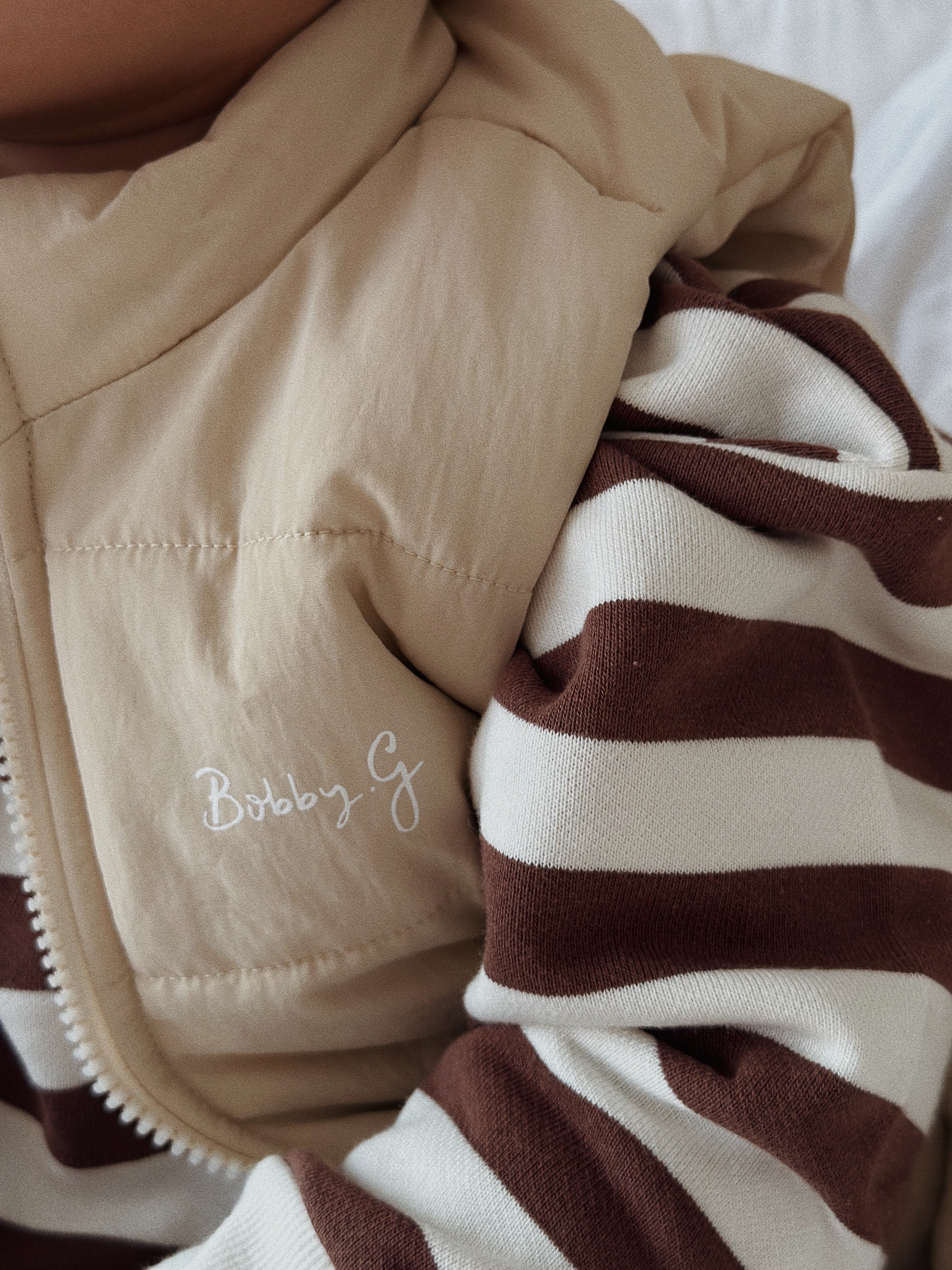 A young toddler wearing the Camden chocolate brown striped pullover and a cream vest over the top.