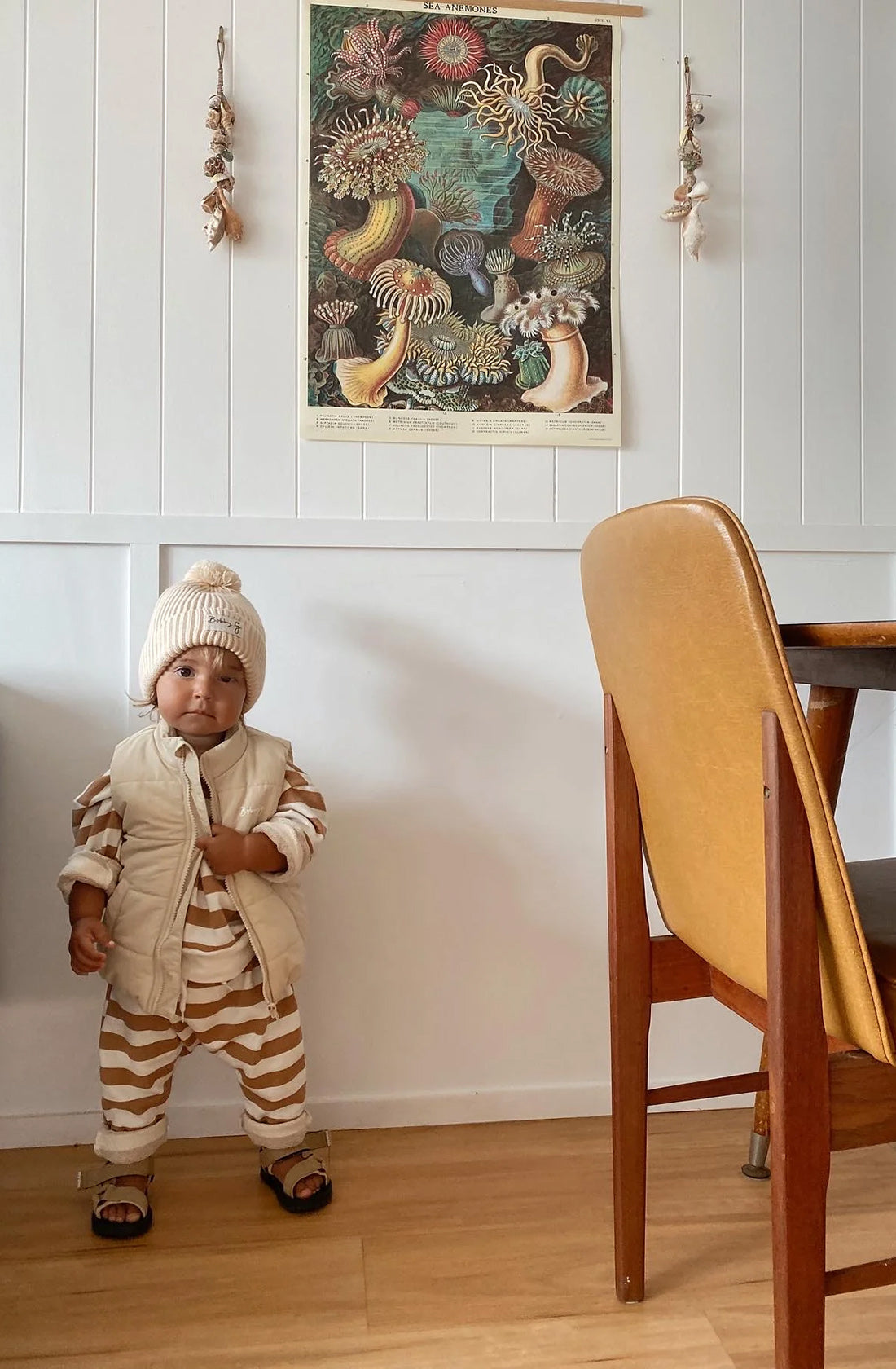 A young toddler wearing the Camden caramel striped pullover and matching pants with a puffer vest over the top an the pom pom beanie in creme.