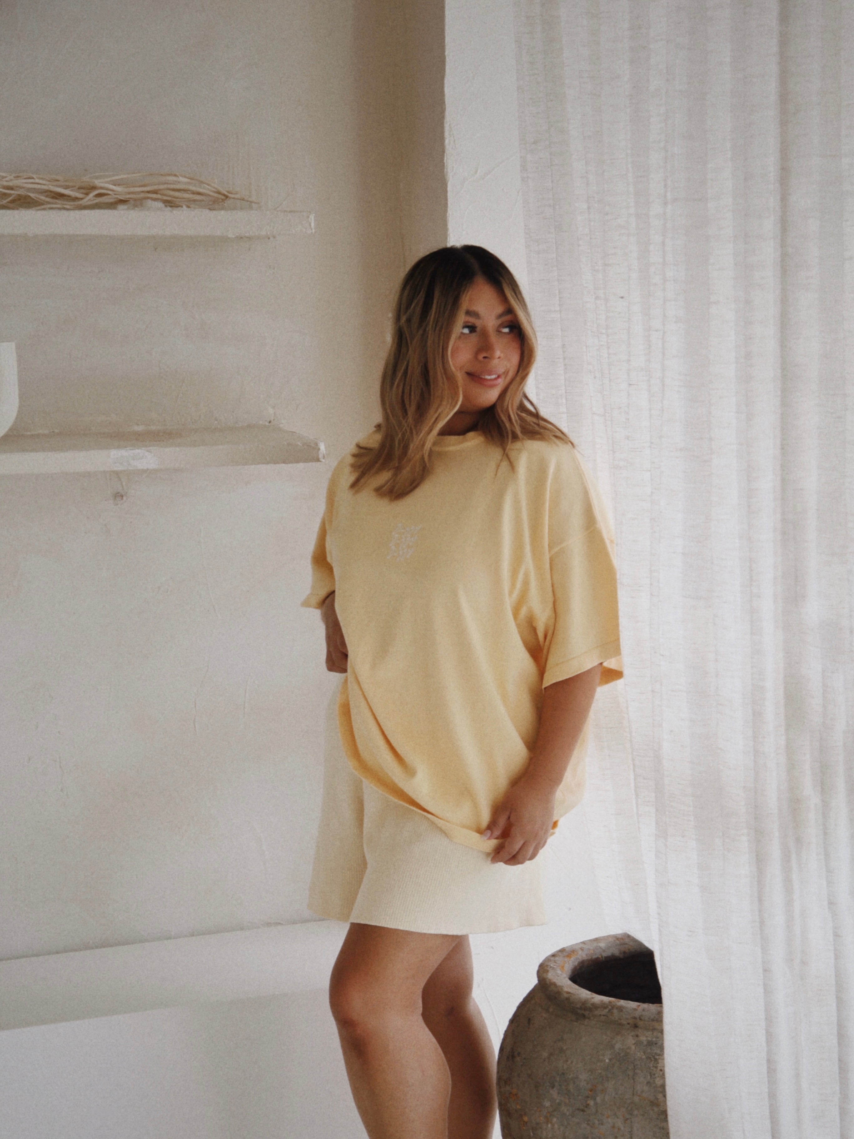 A woman wearing the Women's Signature Tee in Butter by ZIGGY LOU exudes casual elegance with its oversized fit and subtle embroidered logo.