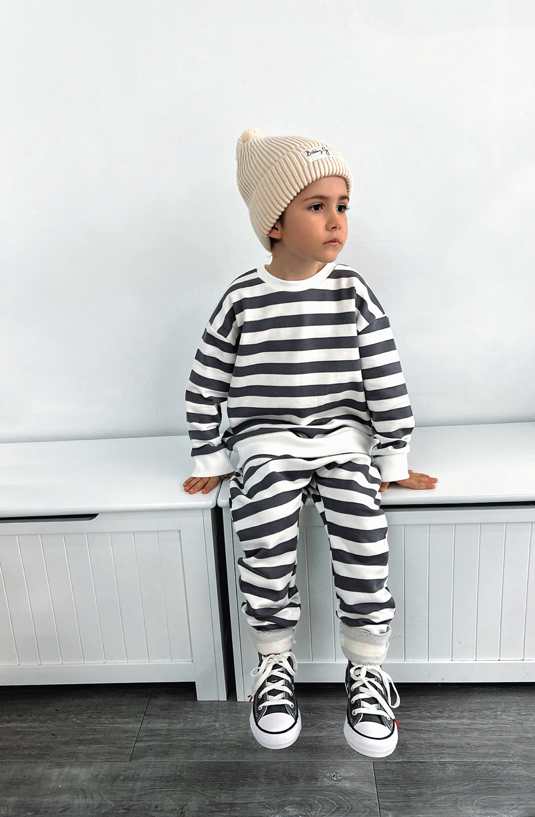 A young boy wearing the Camden navy striped pullover and matching sunny pants with the Bobby G creme beanie