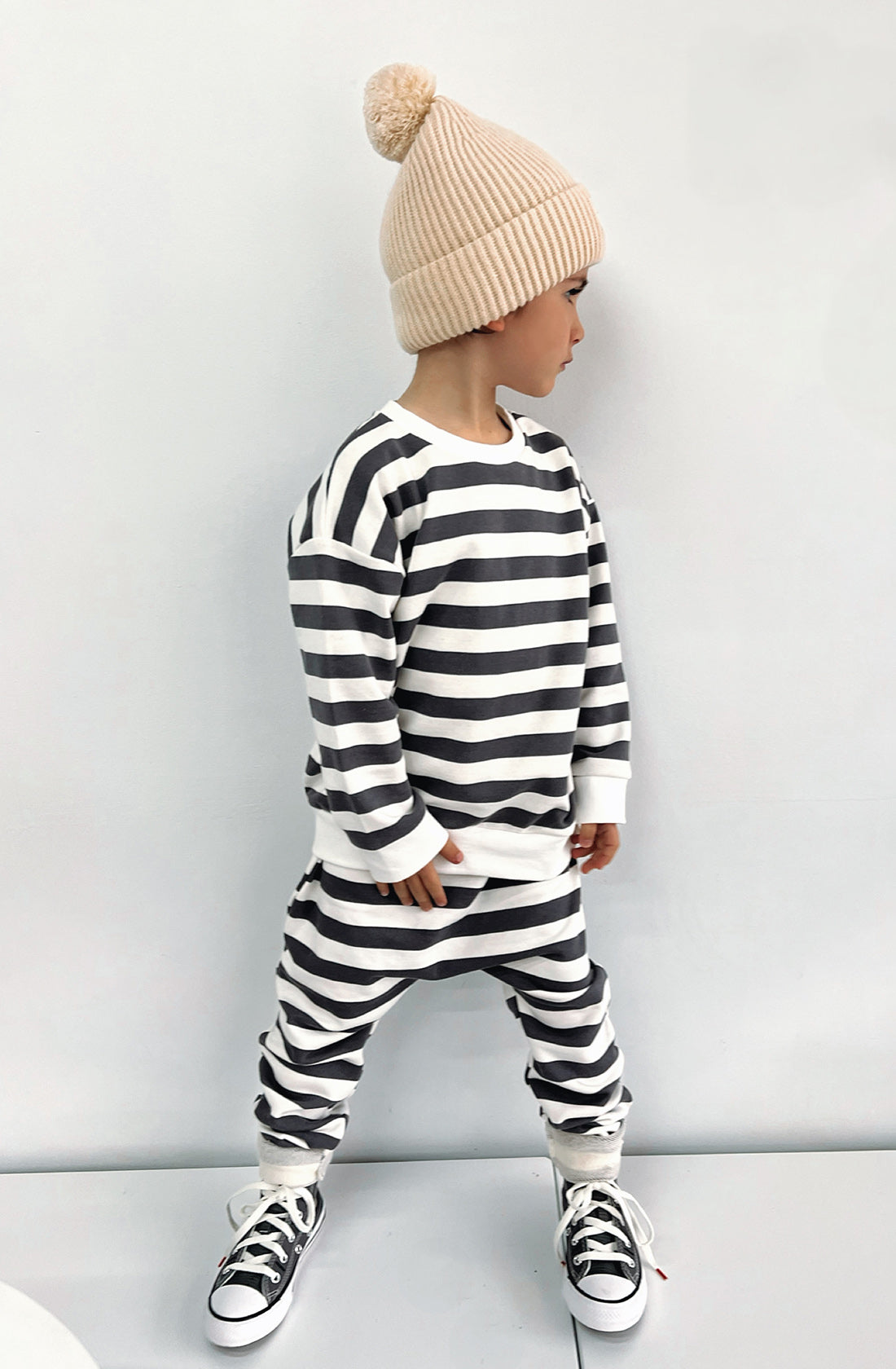 A young boy wearing the Camden navy striped pullover and matching sunny pants with the Bobby G creme beanie.