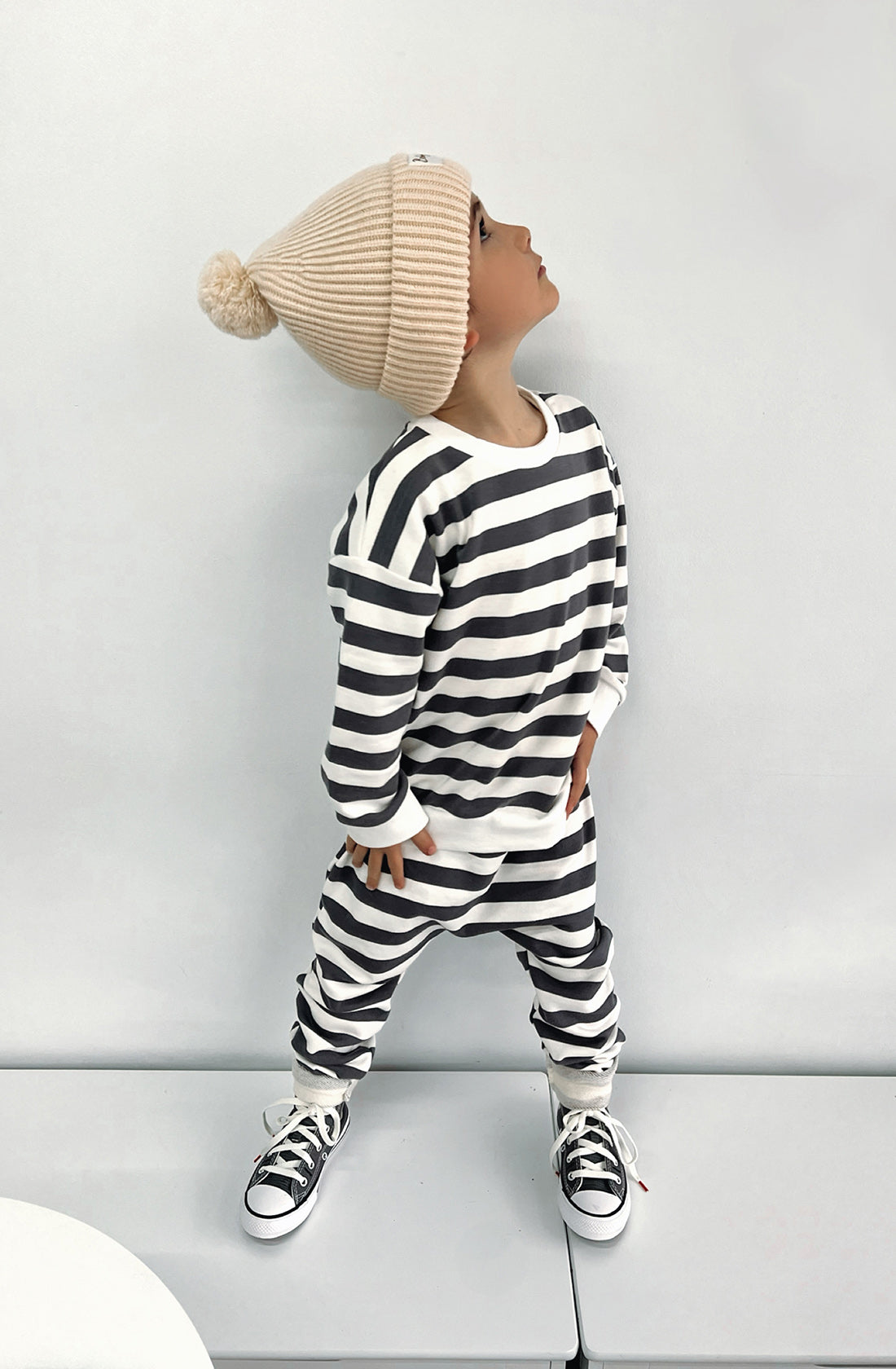 A young boy wearing the Camden navy striped pullover and matching sunny pants with the Bobby G creme beanie