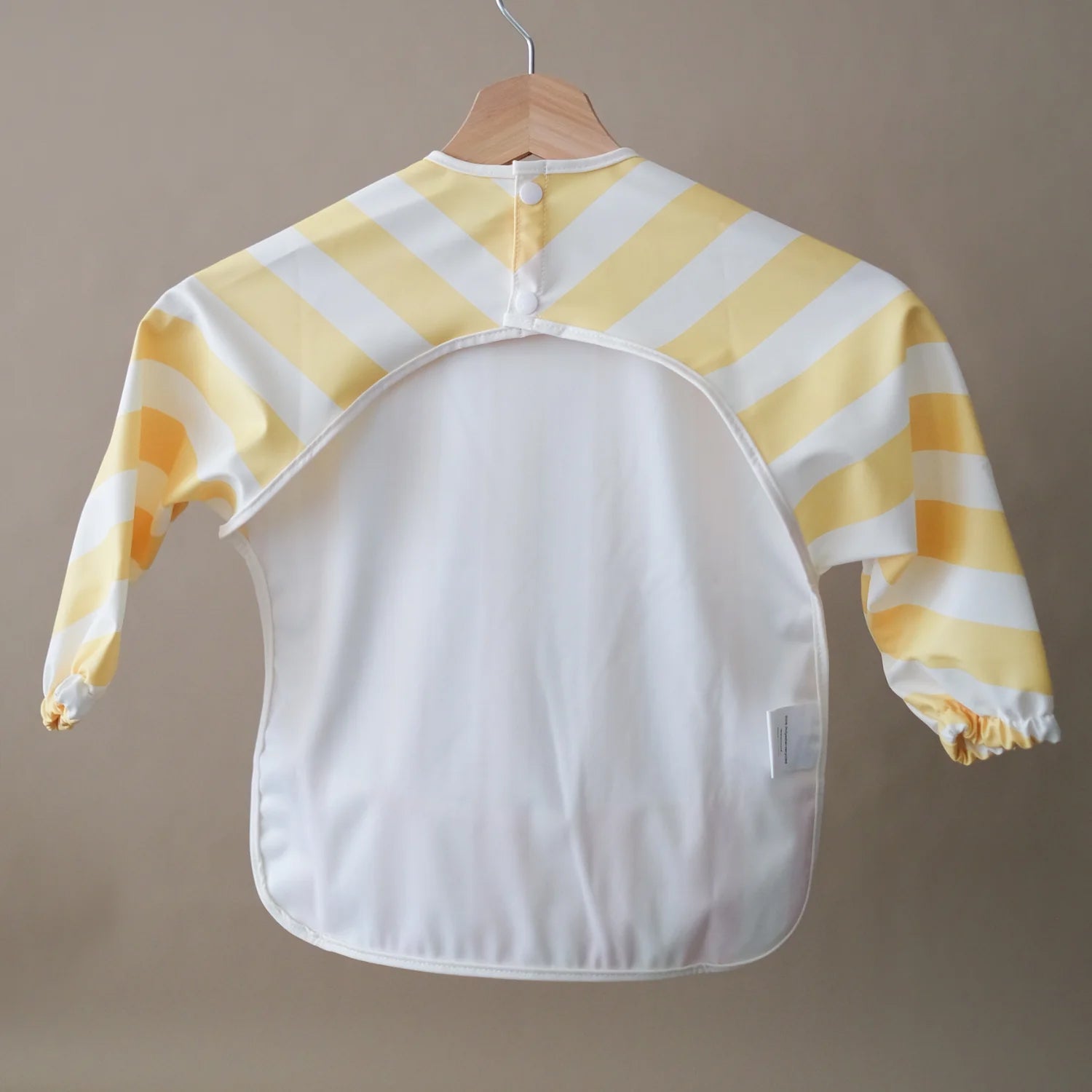 ROMMER Smock Bib in Pina Stripe from the back hanging from a coat hanger.