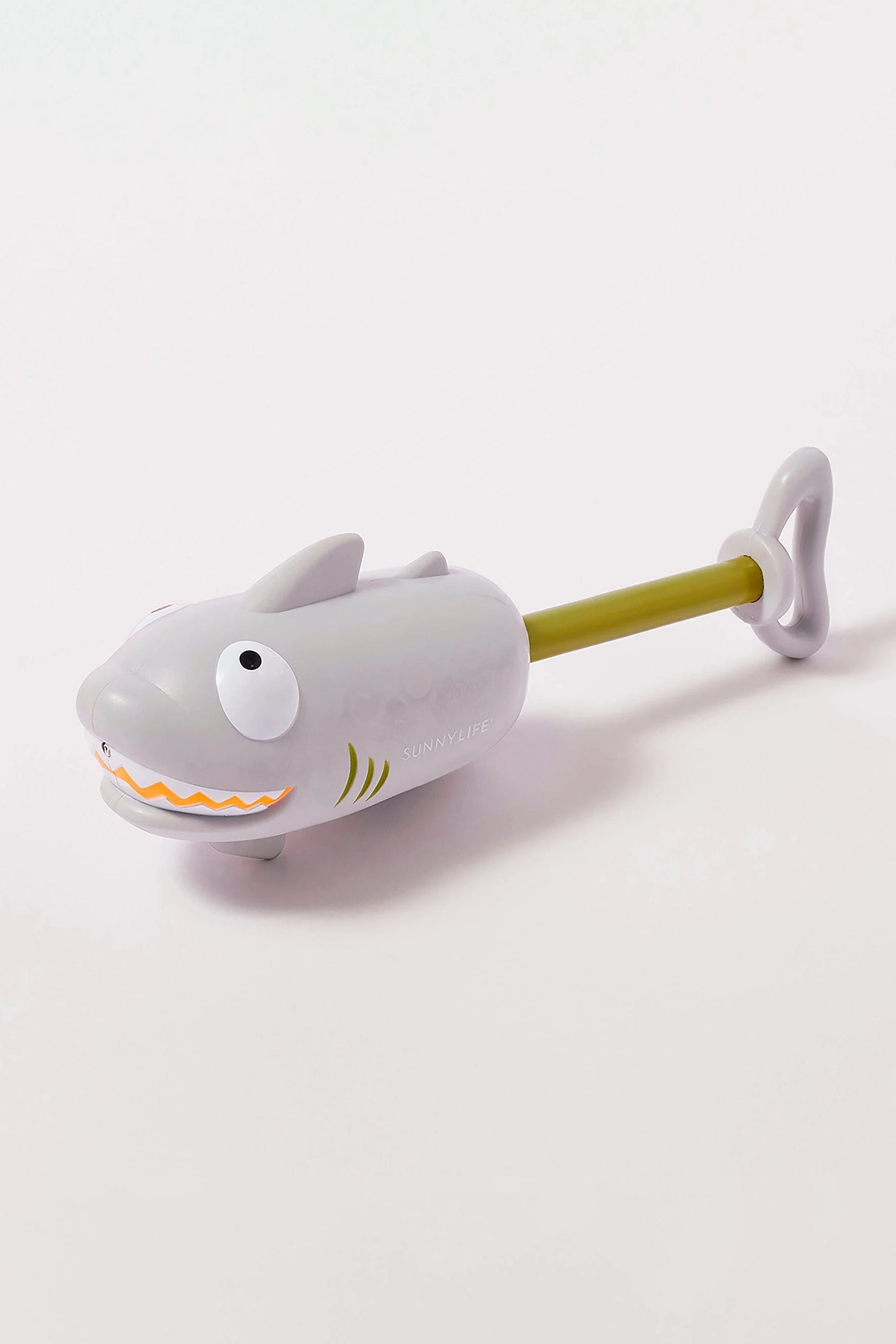 The Shark Water Squirter by SUNNYLIFE, a children's bath toy shaped like a gray shark with cartoonish eyes and an orange zigzag mouth, features a wind-up mechanism with a green handle and key at the end. Resting on a white surface, this playful shark includes a hand pump squirter for maximum soaking capability.