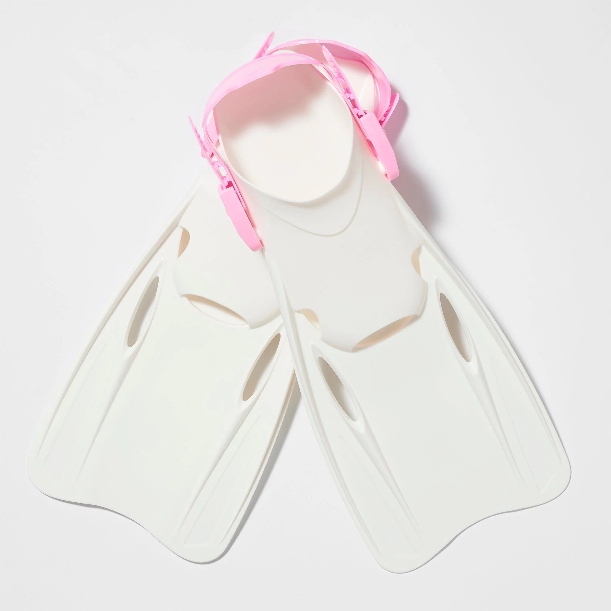 A pair of swimming fins from the SUNNYLIFE Kids Snorkel Set Pink, featuring white bodies with pink adjustable heel straps, are lying on a light surface. These fins have an elongated design with openings near the foot area for efficient water movement, making them perfect to complement your snorkel set.