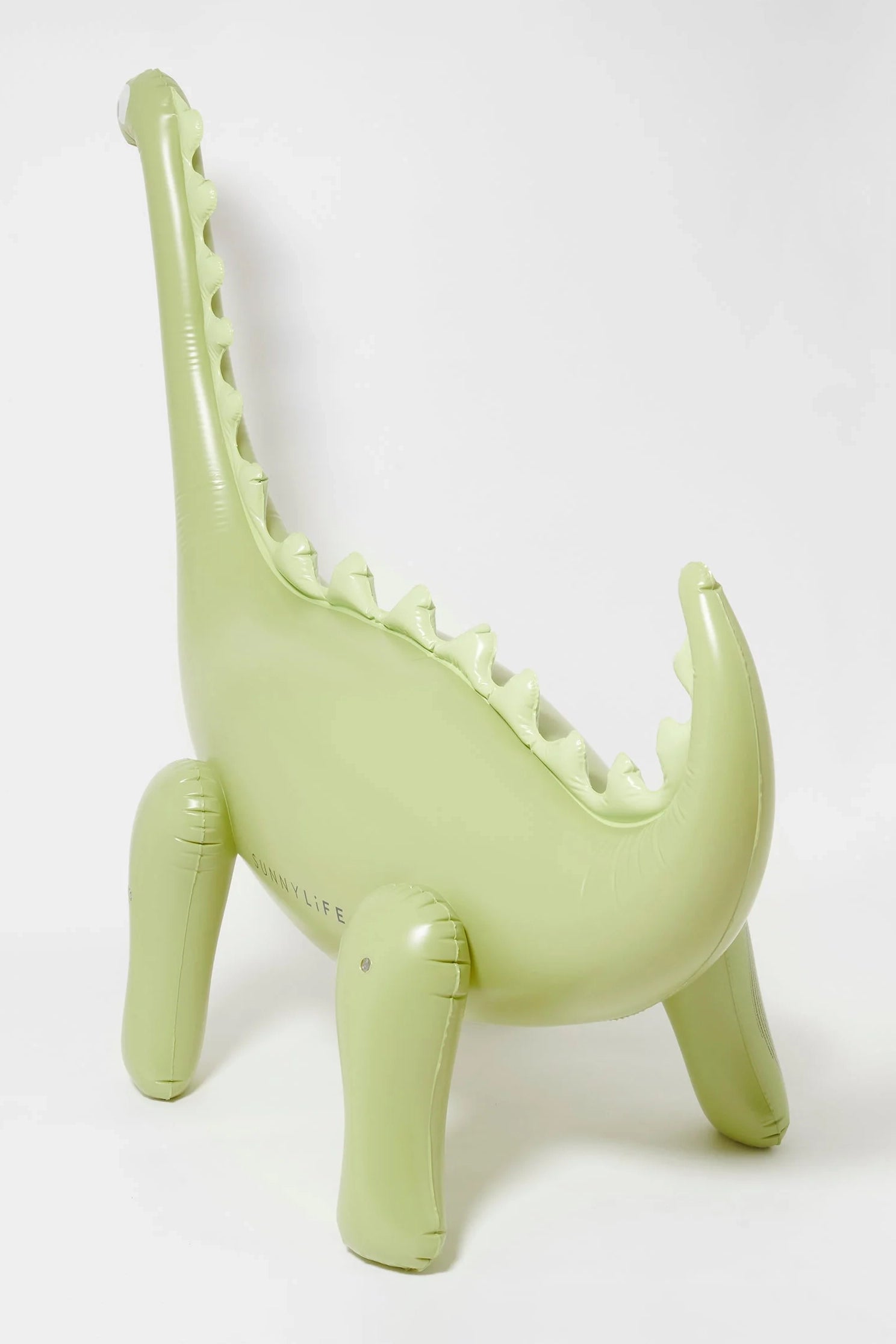 The SUNNYLIFE Dino Giant Sprinkler is a light green inflatable pool toy shaped like a dinosaur featuring four legs, a tail, and a long neck adorned with ridged spikes. Crafted from durable PVC, this playful and friendly design stands upright on a white background. It also includes a repair patch for added convenience.