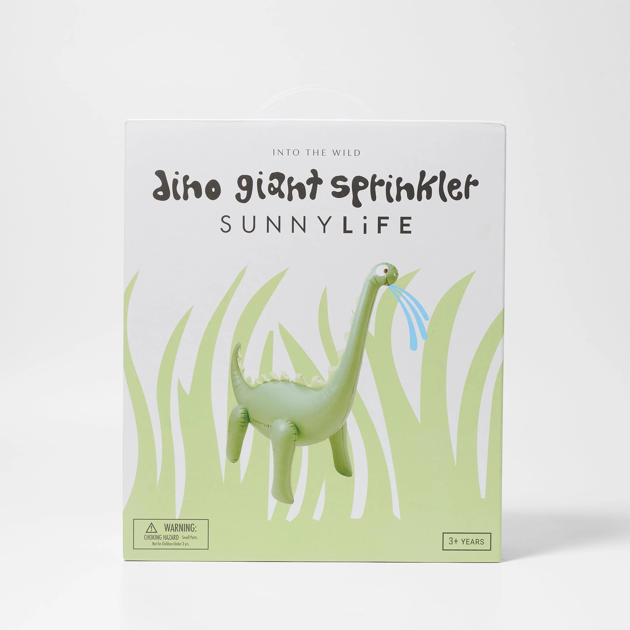 The image displays the packaging of the SUNNYLIFE Dino Giant Sprinkler. The box showcases a playful illustration of a green dinosaur with water spraying from its mouth. Crafted from durable PVC, it comes with a garden hose adaptor and is suitable for children aged 3 and up. The design is framed by stylized grass graphics.