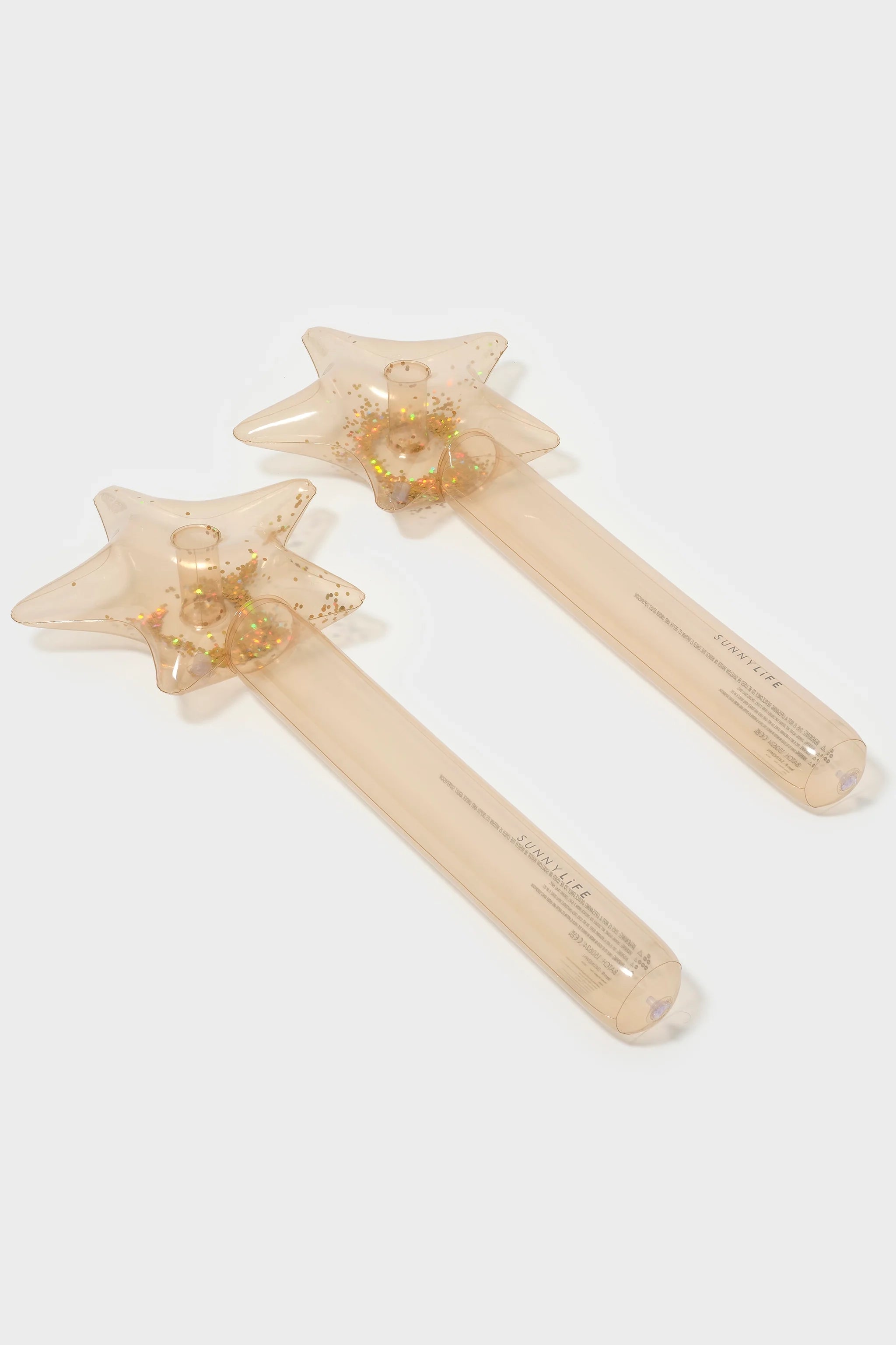 Two star-shaped, transparent facial roller massagers filled with small gold star confetti are known as the Inflatable Star Wands (Set of 2) by SUNNYLIFE. Made of phthalate-free PVC, the massagers feature long, clear handles imprinted with the brand name and rest on a white background.