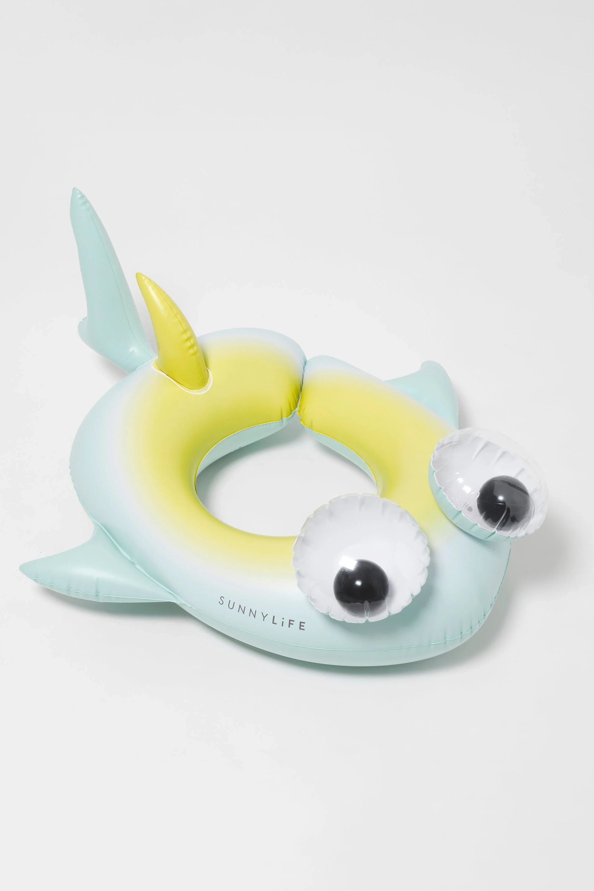 Introducing the Kids Tube Pool Ring Salty the Shark by SUNNYLIFE: a playful inflatable swim ring shaped like a whimsical fish, featuring large, bulging eyes, a small dorsal fin, and a gradient of pale blue to yellow. Crafted from durable PVC with "SUNNYLIFE" printed on the front. Comes with a repair patch for quick fixes.