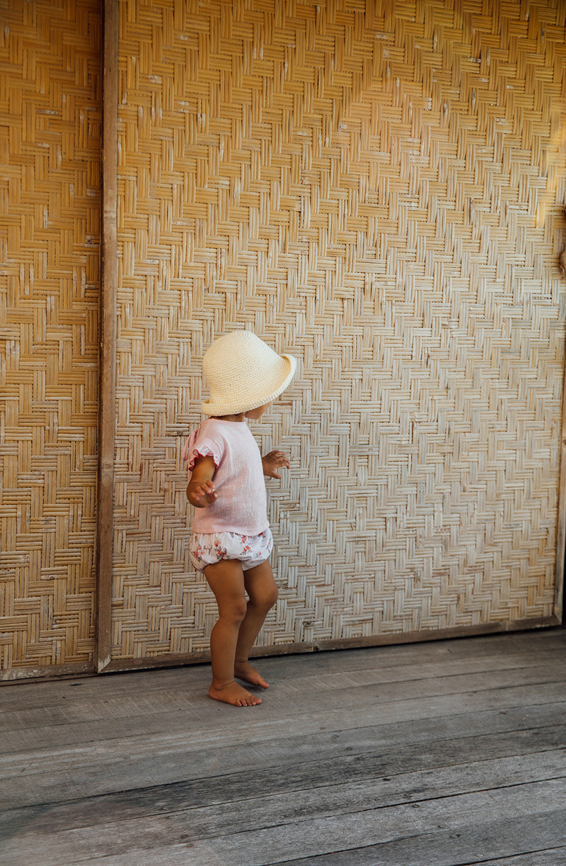 Side view of toddler girl in balinese hut wearing the Penny blouse tucked into Vali bloomers