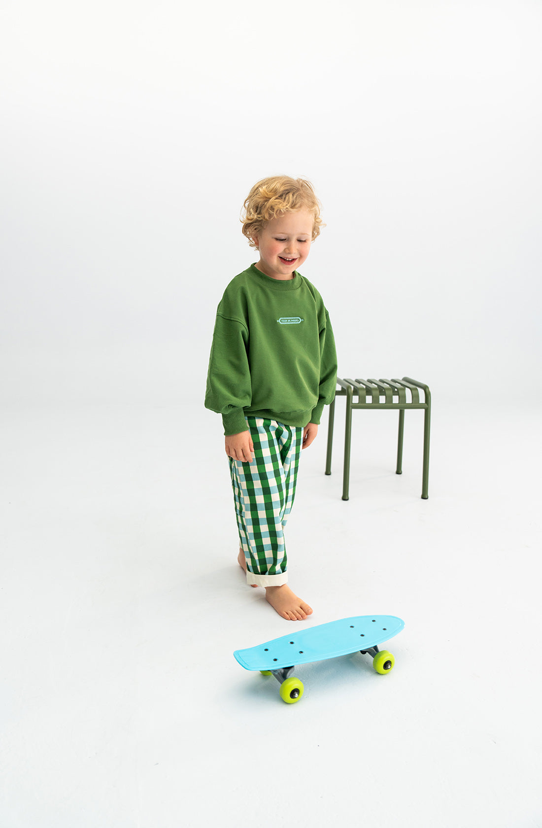 A young boy playing with a skateboard wearing the tour de parks sloppy joe in green.