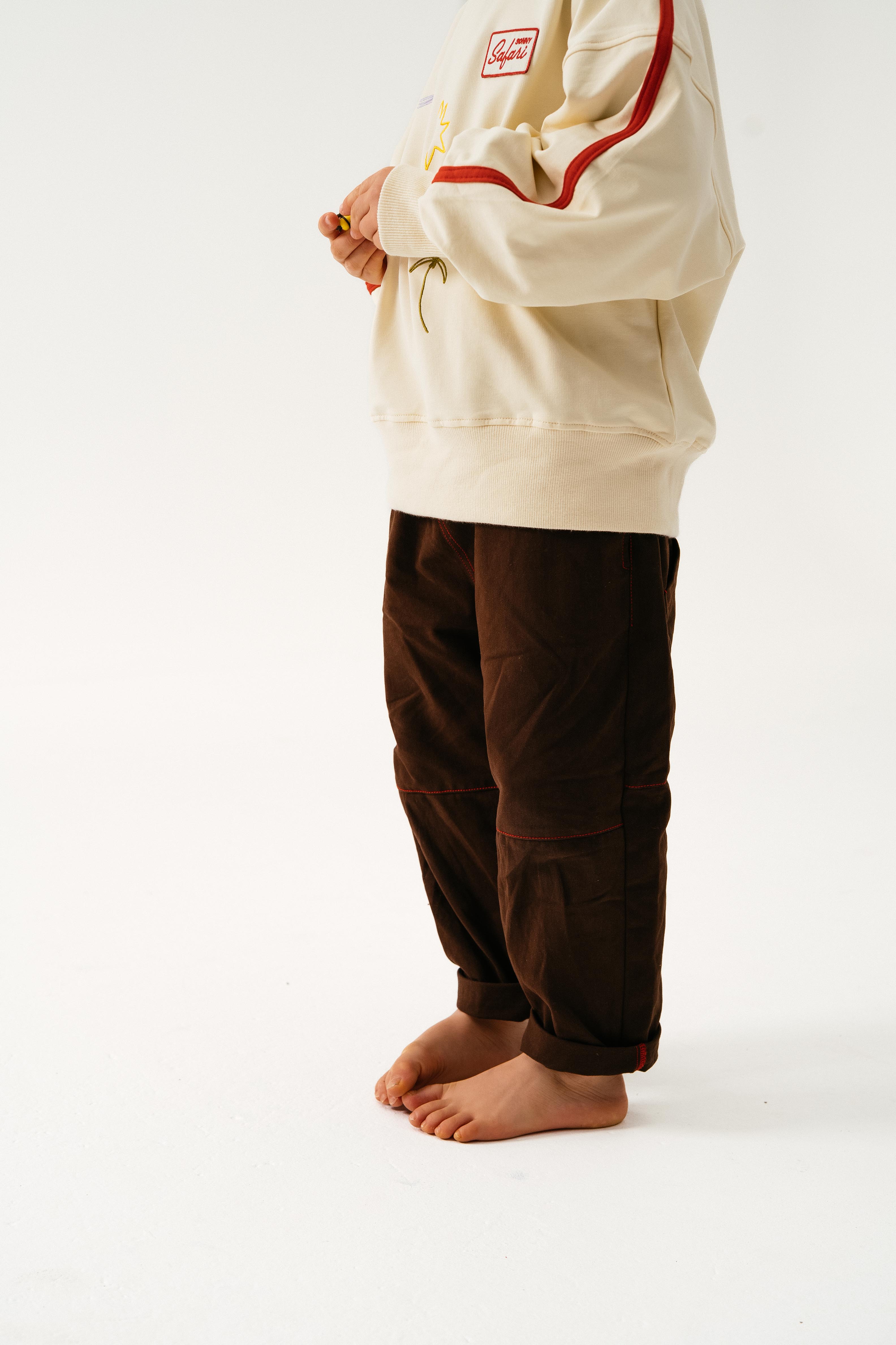 A person stands barefoot on a white surface, wearing Sonny Label - Cargo Pants by SONNY LABEL. The loose cotton twill pants are paired with a cream sweatshirt with red stripes, and the image is cropped at the shoulders to hide their face.