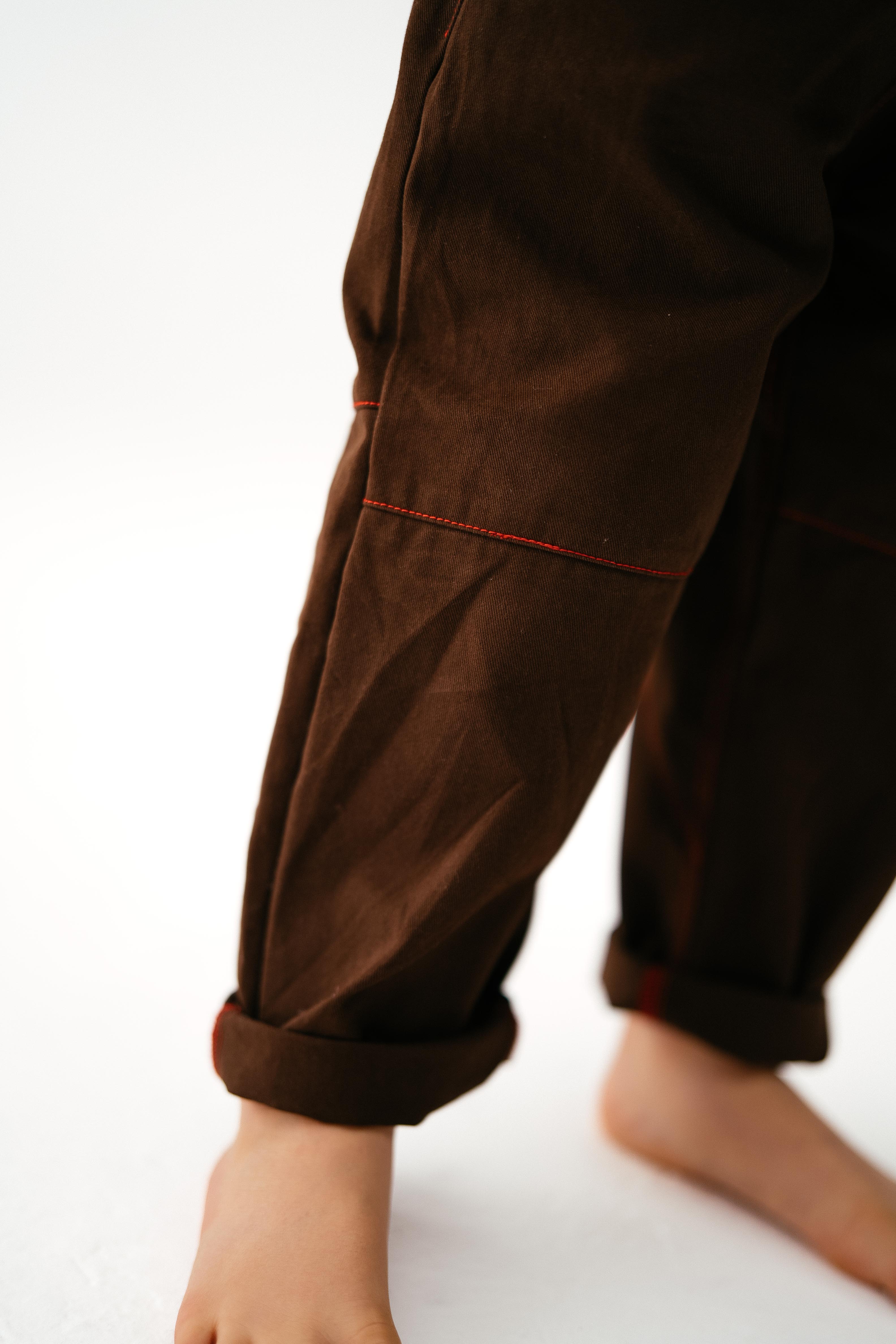 A close-up shows a person’s bare feet and lower legs wearing SONNY LABEL Sonny Label - Cargo Pants with loose legs, red stitching, and cotton twill fabric, standing on a white surface.