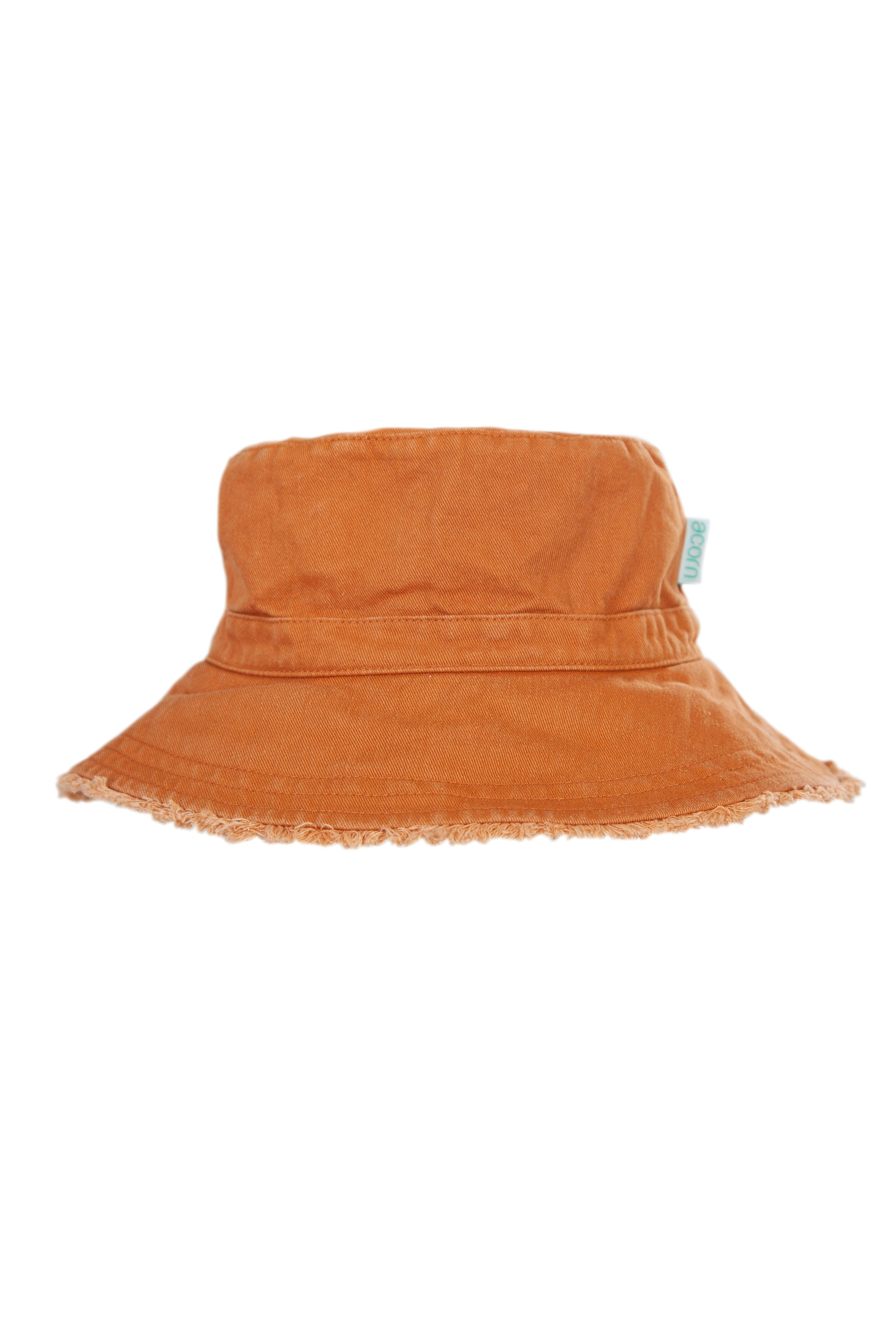 The Frayed Bucket Hat Chestnut from ACORN KIDS is a lightweight cotton twill hat with an orange hue, featuring a wide, slightly frayed brim and offering UPF50+ sun protection. Its casual design makes it perfect for sunny weather, and a small tag is visible on the side.