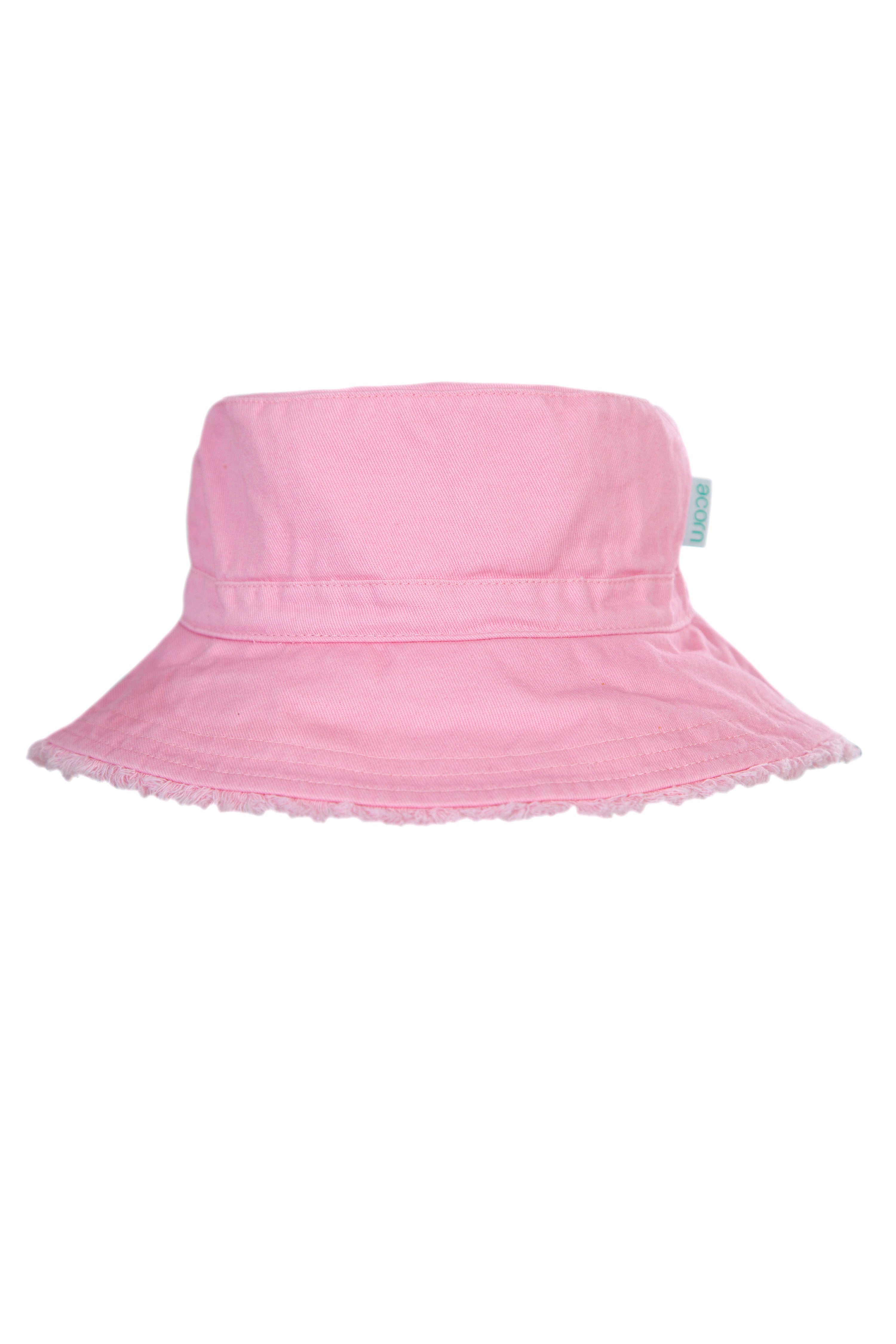 The Frayed Bucket Hat Strawberry by ACORN KIDS is a pastel pink bucket hat made from Cotton Twill with a wide brim that provides UPF50+ sun protection. It includes a subtle, matching band around the crown and a small, off-white tag on the side. The brim's edge is slightly frayed, giving it a casual, worn-in appearance.