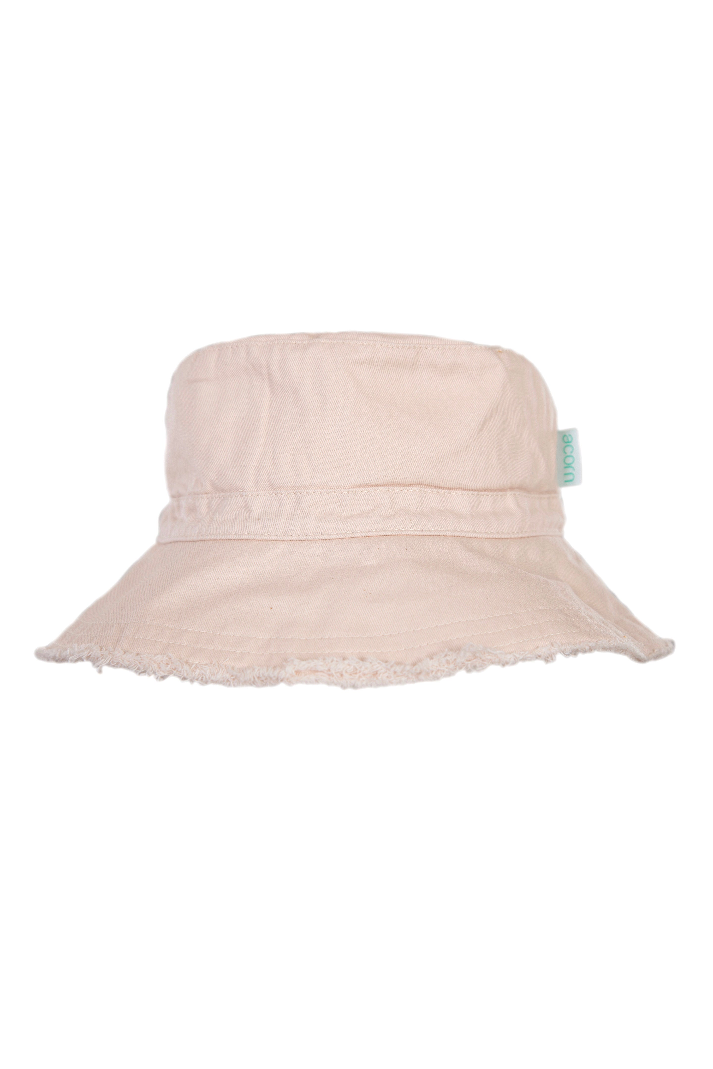 The Frayed Bucket Hat Vanilla by ACORN KIDS is a vanilla-colored bucket hat featuring a slightly frayed brim and a cloth tag with a blue logo on the side. Made from soft, lightweight cotton twill, it also offers UPF50+ sun protection. The background is plain and white.