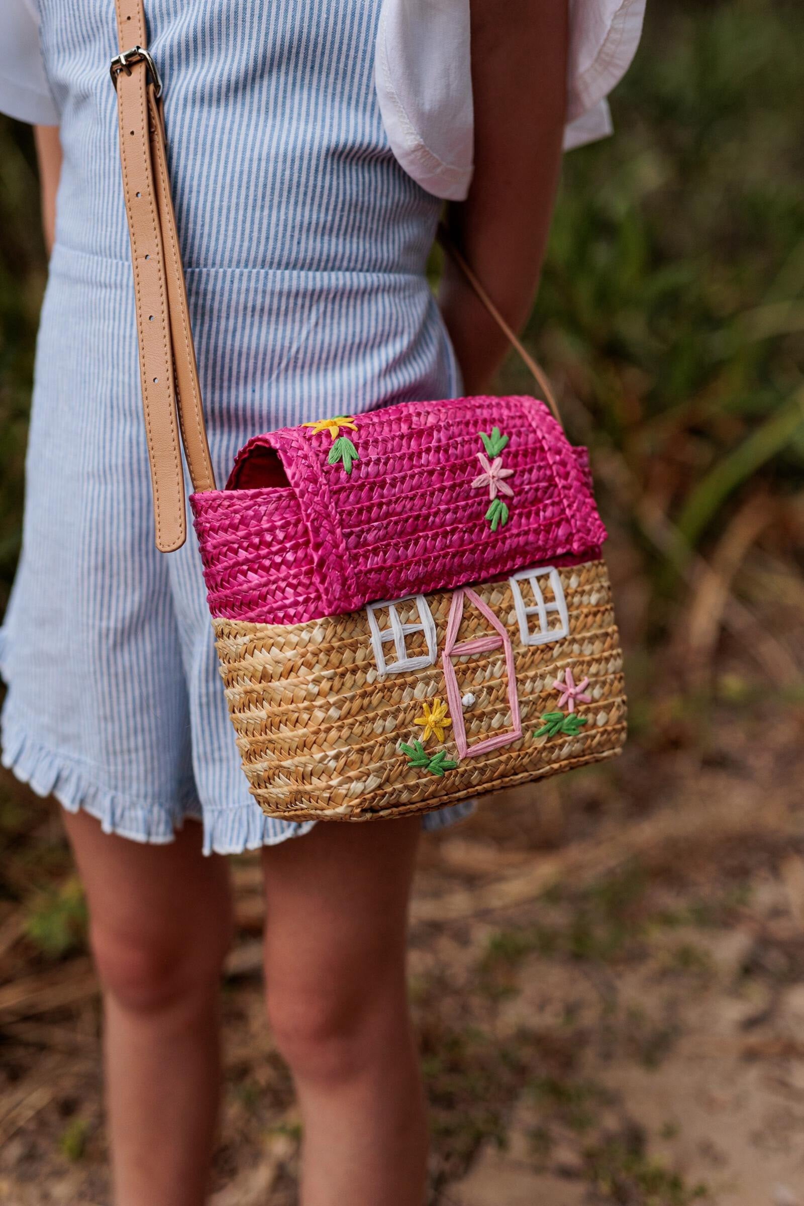 A young girl wearing the La Maison Straw Bag by Acorn Kids.