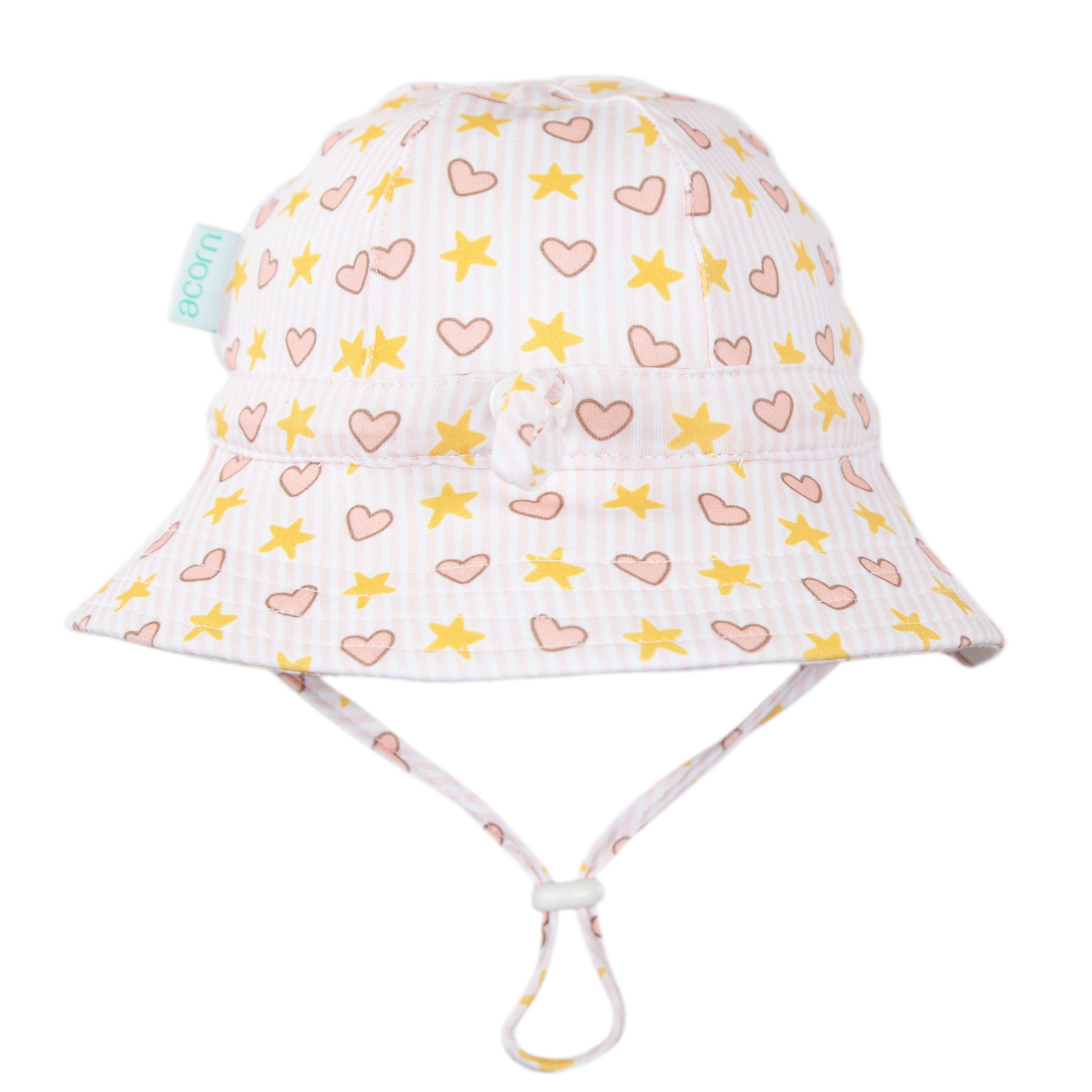 The Acorn Kids - Love and Stars Stretch Cotton Wide Brim Sunhat by ACORN KIDS is a light pink cotton jersey hat with yellow stars, pink hearts, UPF50+ protection, an adjustable chin strap, and a side fabric tag.