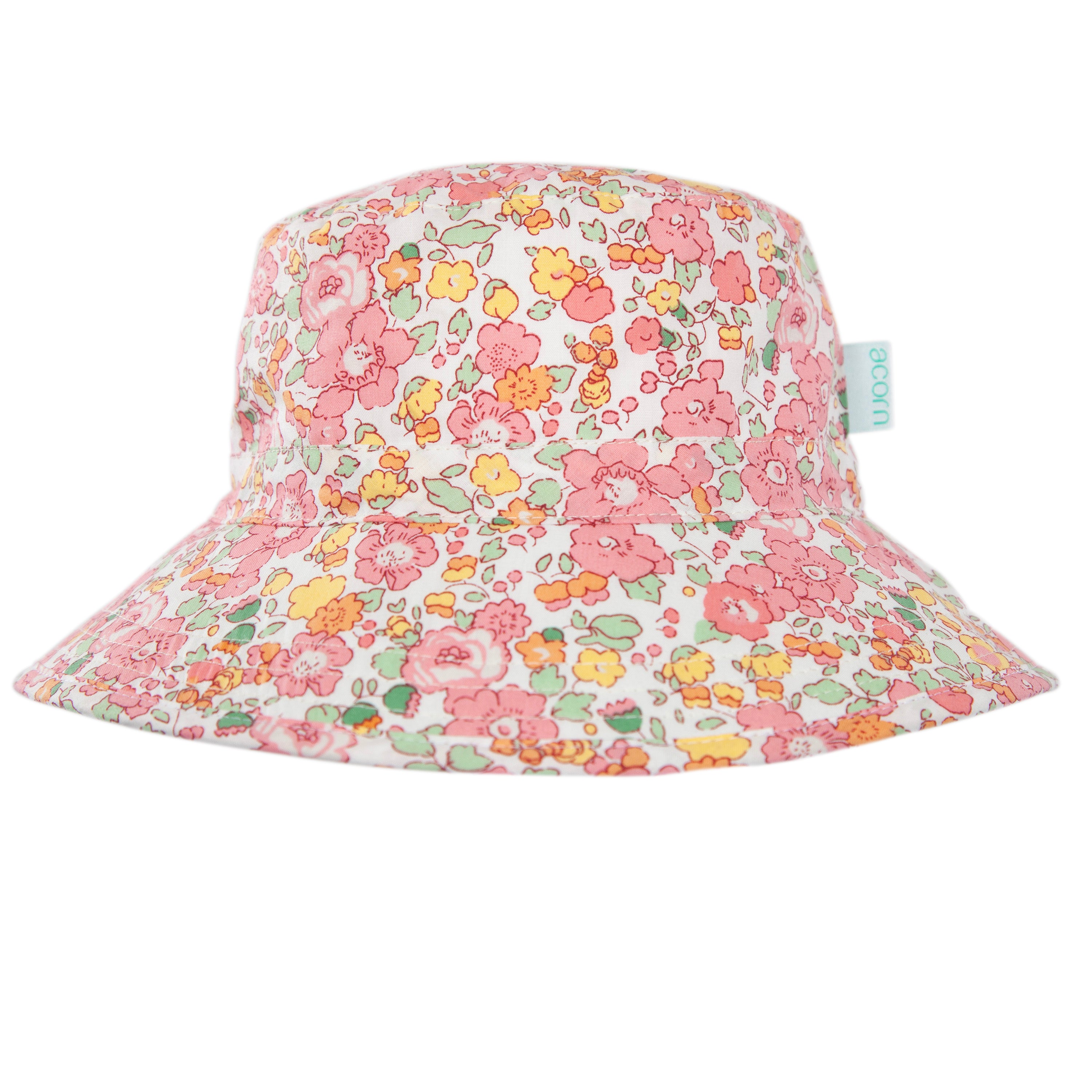 The Acorn Kids - Tessa Broad Brim Bucket Hat by ACORN KIDS features a pink floral pattern in yellow and green on white, UPF50+ sun protection, and a small blue side tag with white text.