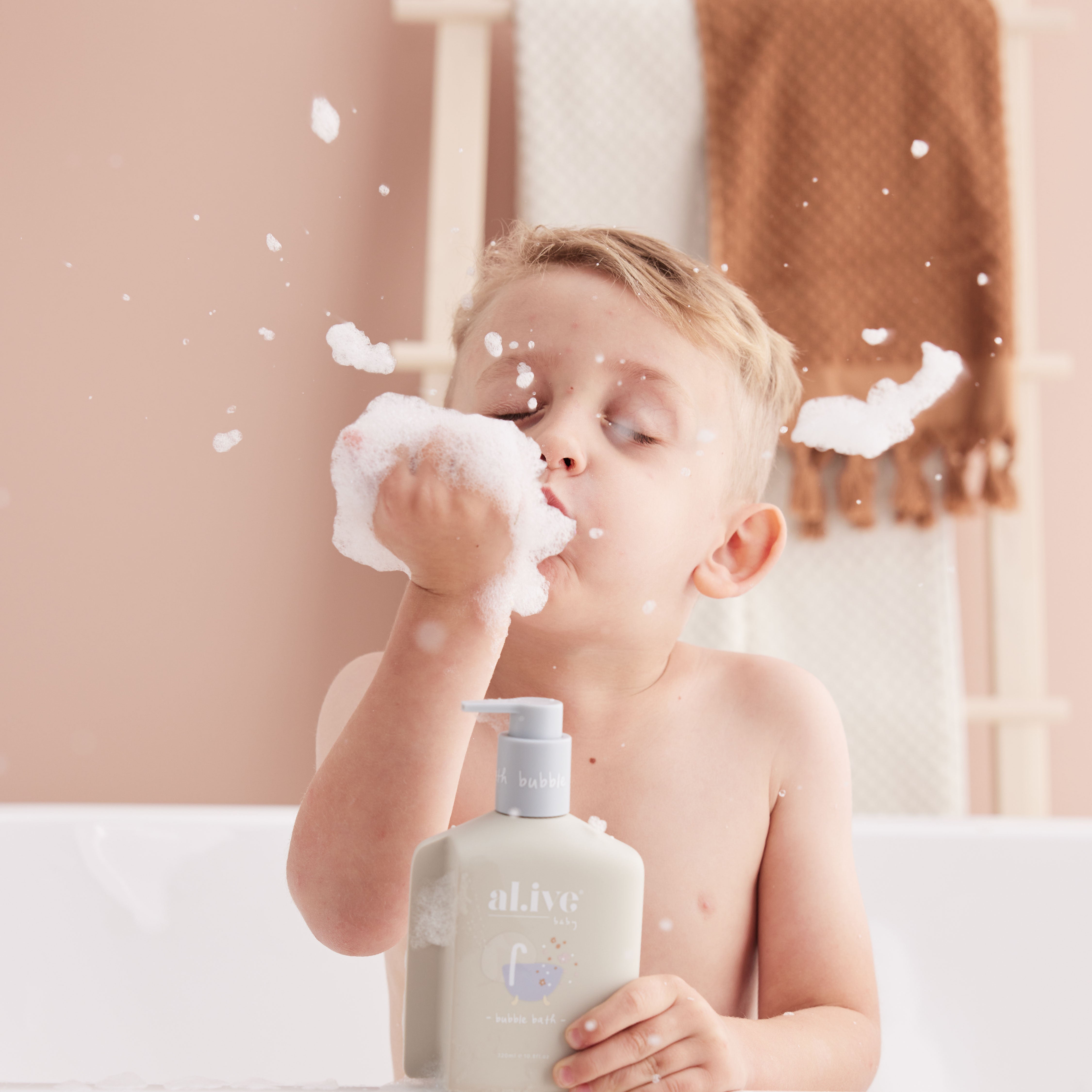 A young boy blowing bubbles of soap from his hand in the bath holding the apple blossom bubble bath by al.ive body.