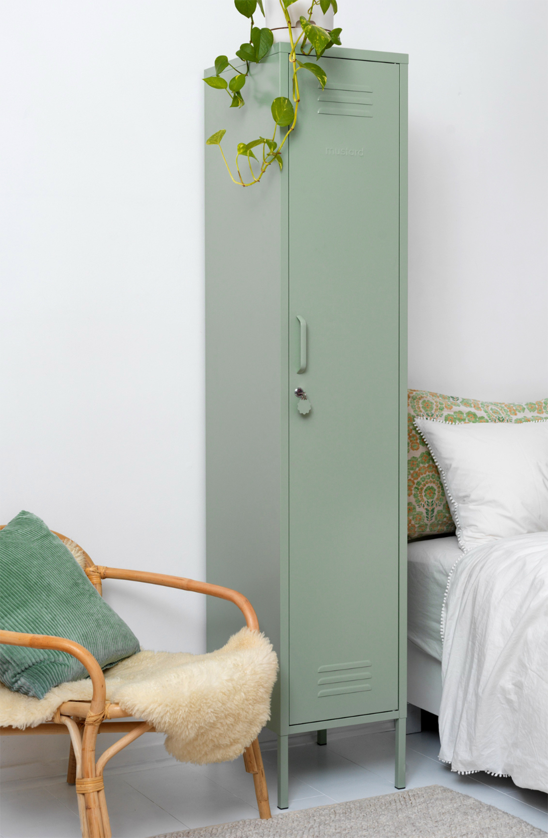 The skinny locker in sage next to a bed.